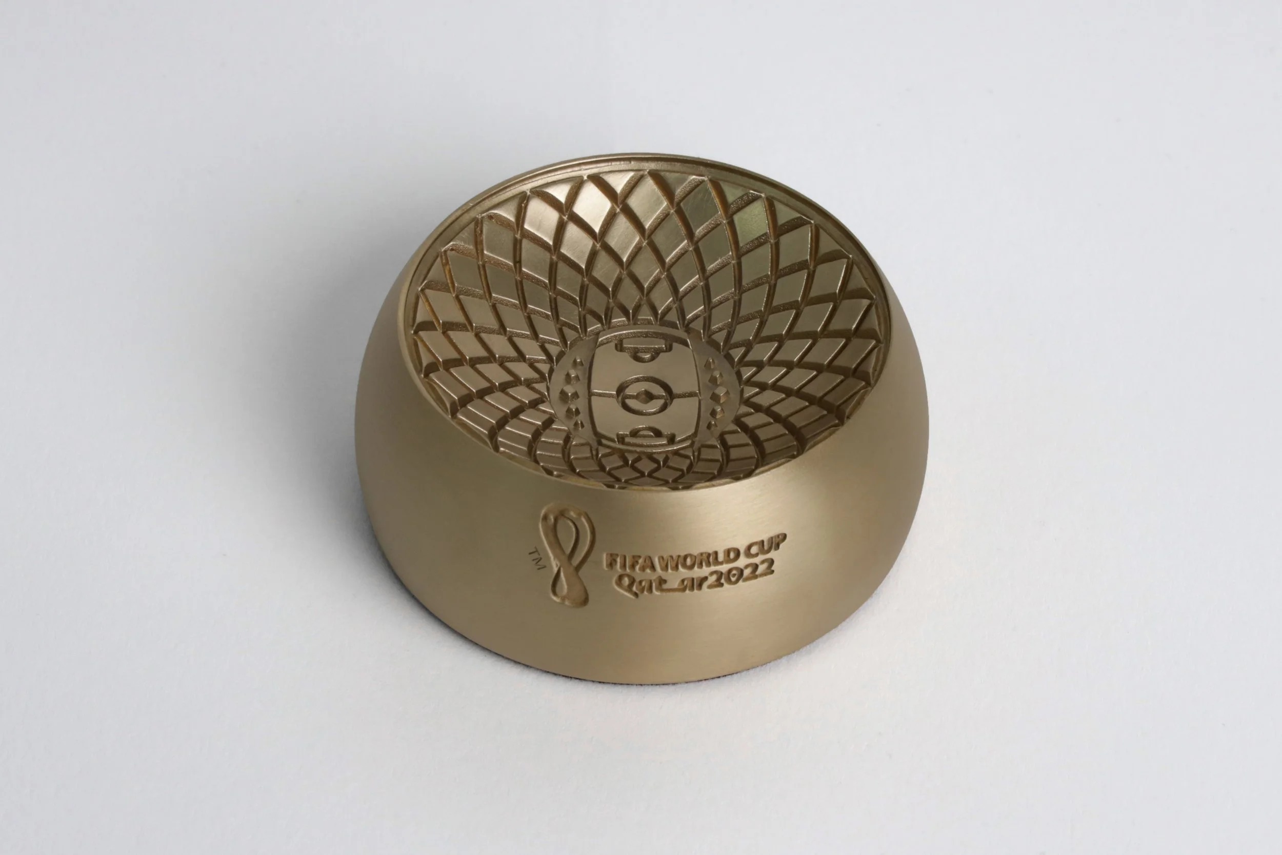 Gold-colored FIFA World Cup Qatar 2022 trophy with intricate design, positioned on a plain white surface.