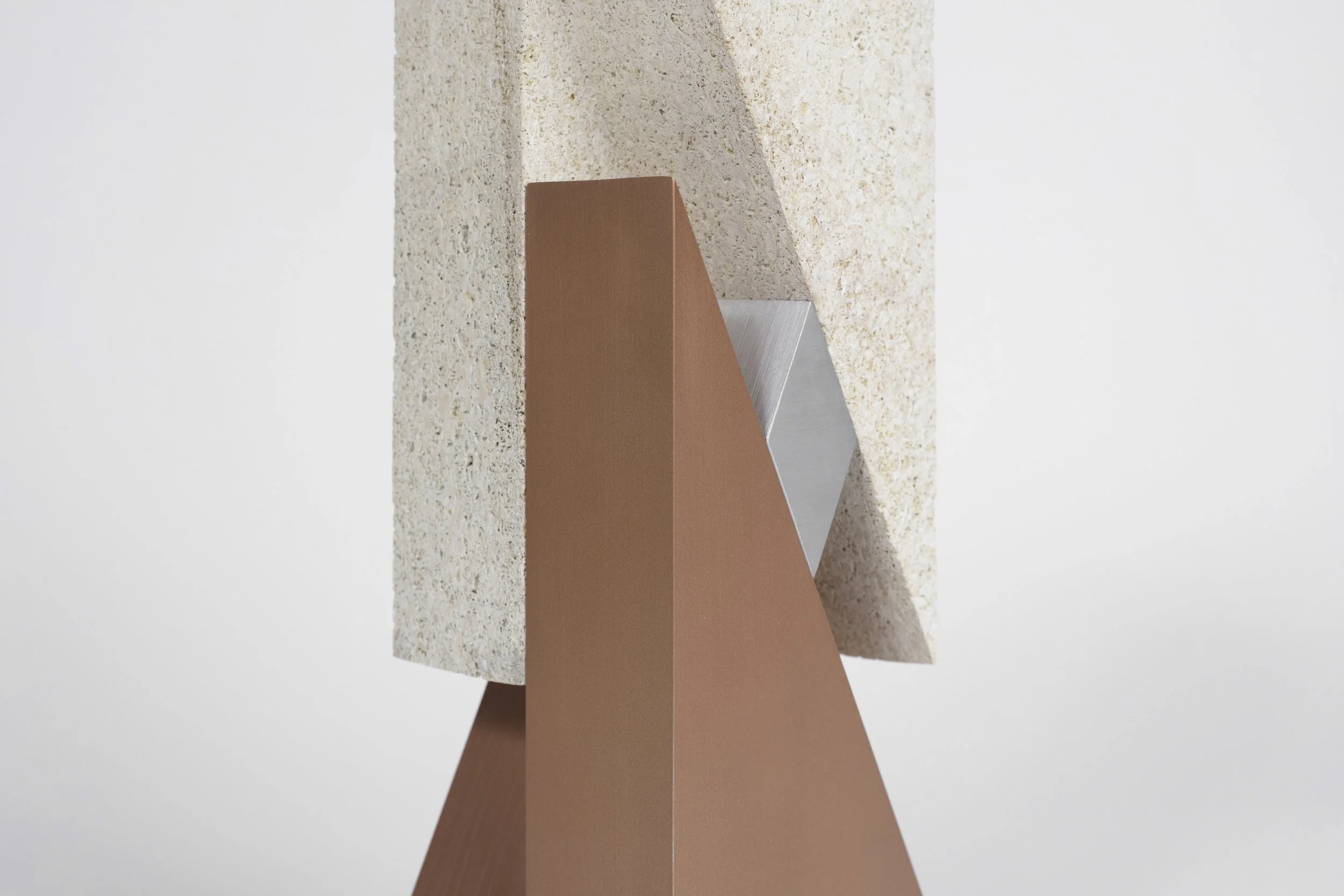 A modern abstract sculpture with geometric shapes, made of textured pink, gray, and beige materials, against a plain white background.
