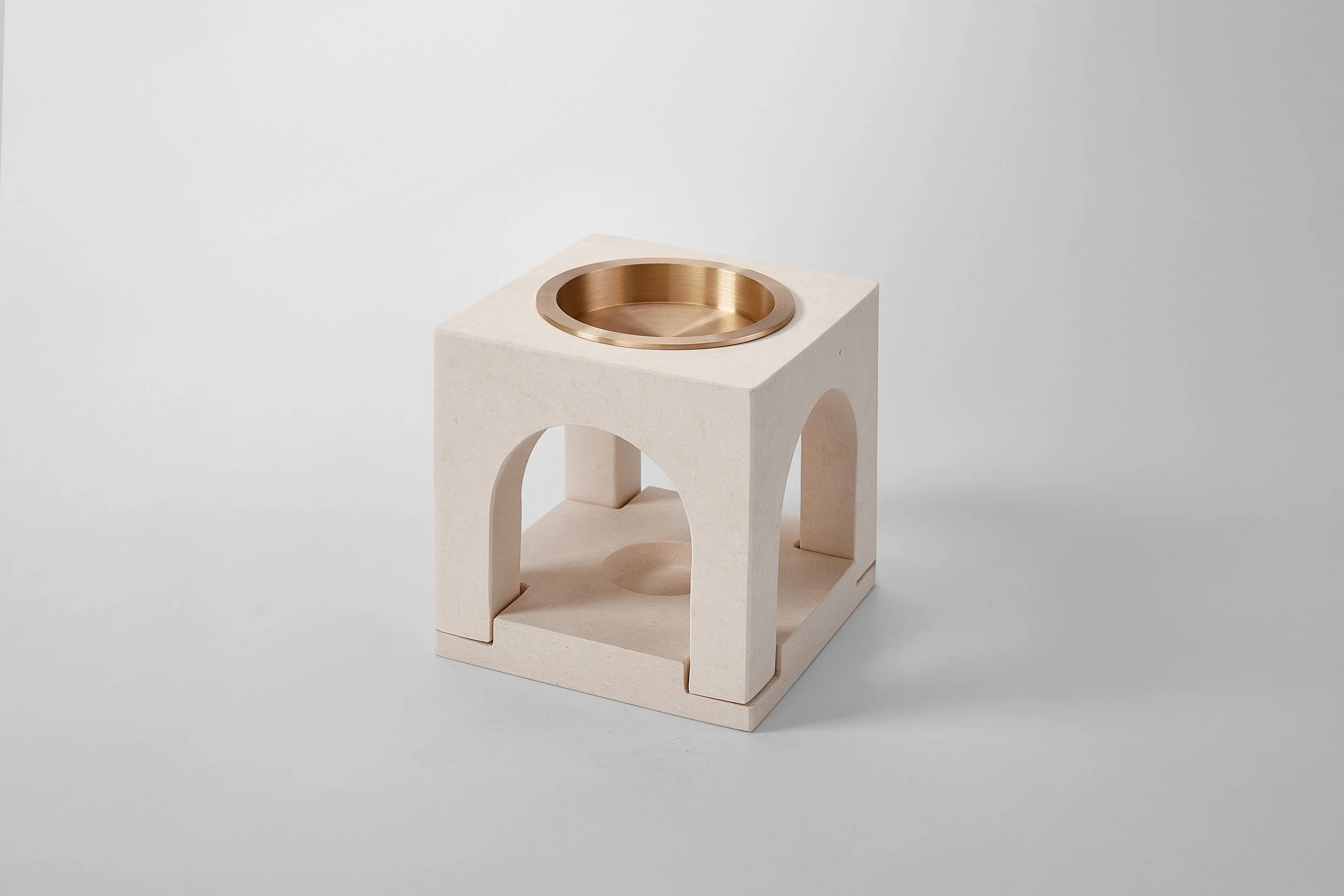 A modern decor piece with a square white base and a round brass inset on top, situated on a plain light background.