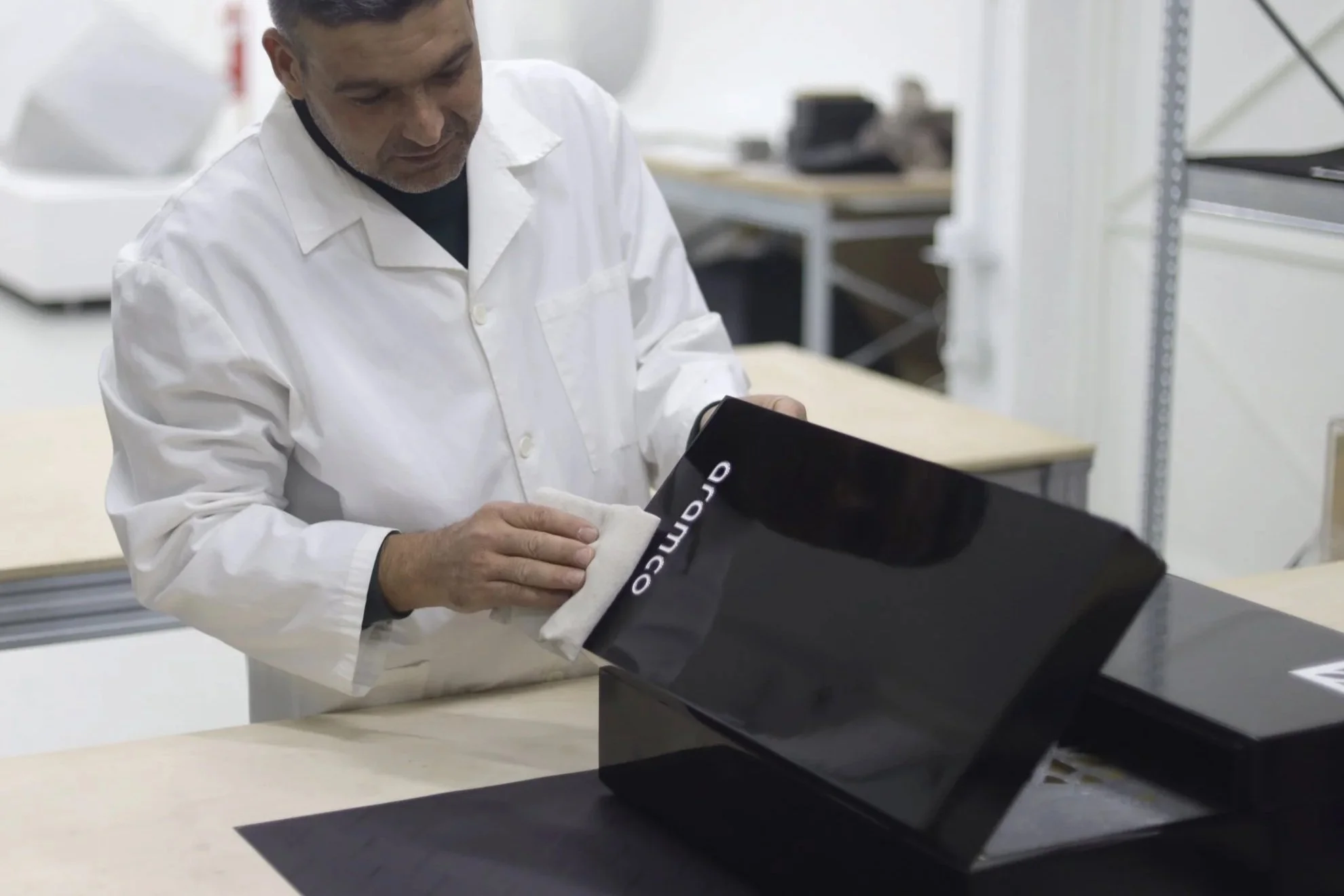 A technician in a white lab coat cleaning a black tennis shoe with a white cloth in a laboratory setting.