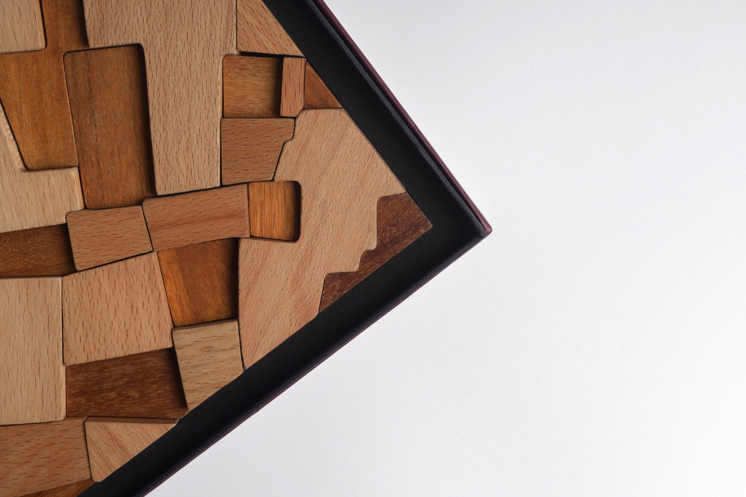 Close-up of a wooden puzzle or parquet pattern on a surface, with various shades of brown and a black border, against a white background.
