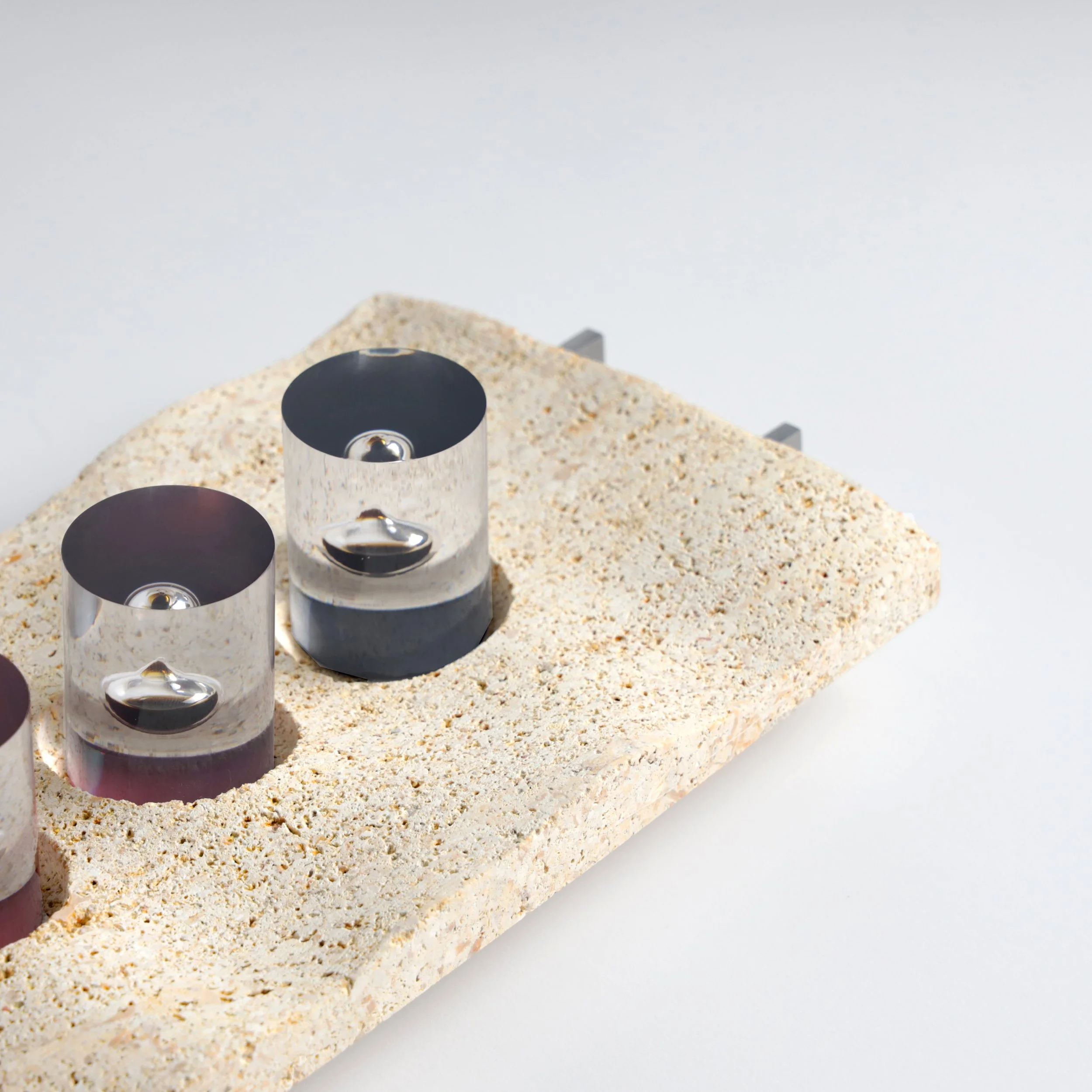 Close-up of small metallic objects with round black tops positioned on a sandy surface with a plain white background.