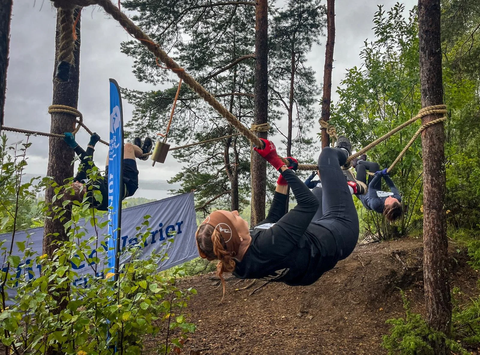 Kilpailijat roikkumassa puussa Tampereella järjestettävässä urheilutapahtumassa nimeltä Mountain Warriors. Kilpailijat liikkuvat eteenpäin puiden väliin kiinnitetyillä köysillä.