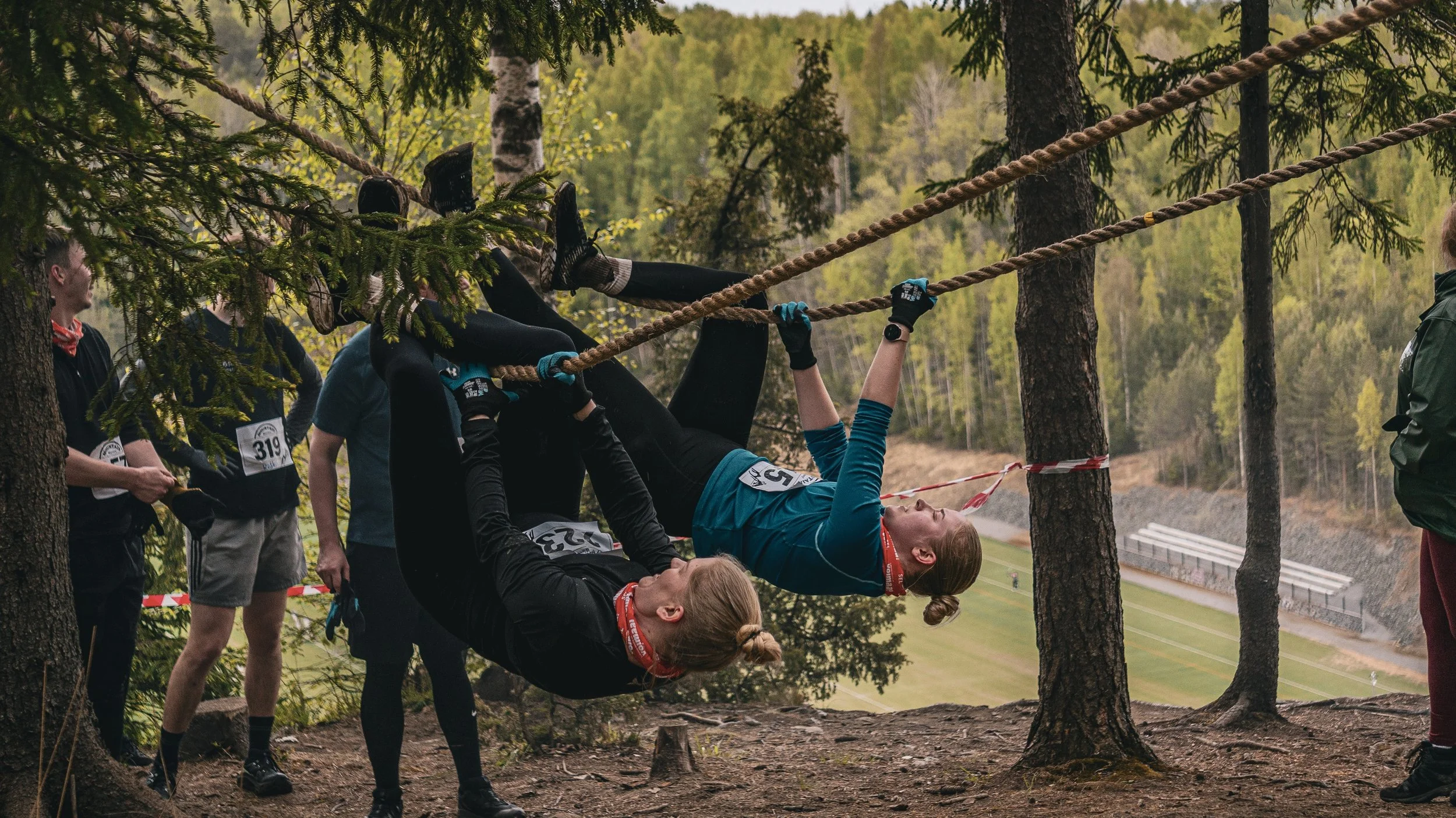 Ihmiset kiipeävät köysiä estejuoksutapahtumassa ulkona luonnossa.