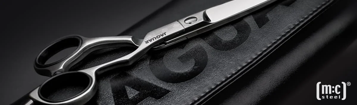 Close-up of hairdressing scissors on a black cutting board with a black leather cover, with the brand name 'Jaguar' visible.