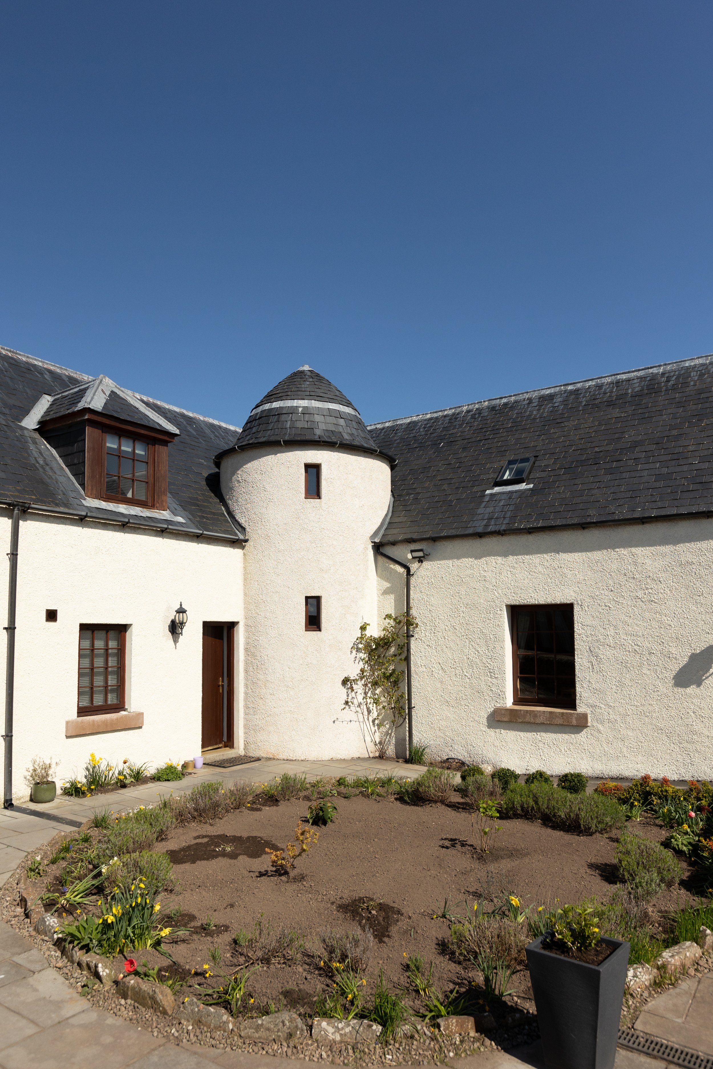 Exterior of a white, stucco house with a conical tower, slate roof, windows, and a courtyard garden.
