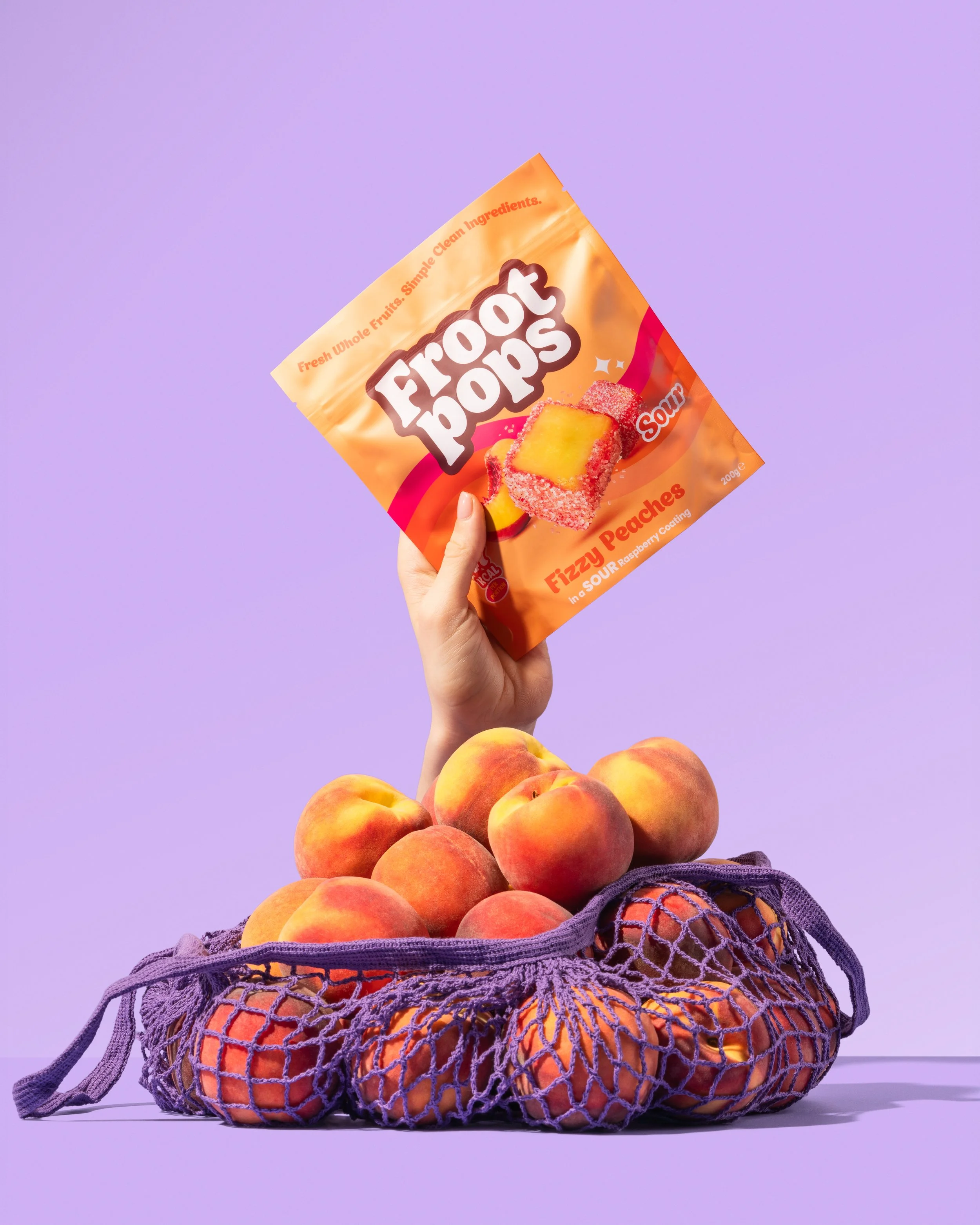 A hand holding a bag of Froot Pops fizzy peaches in a sour raspberry coating