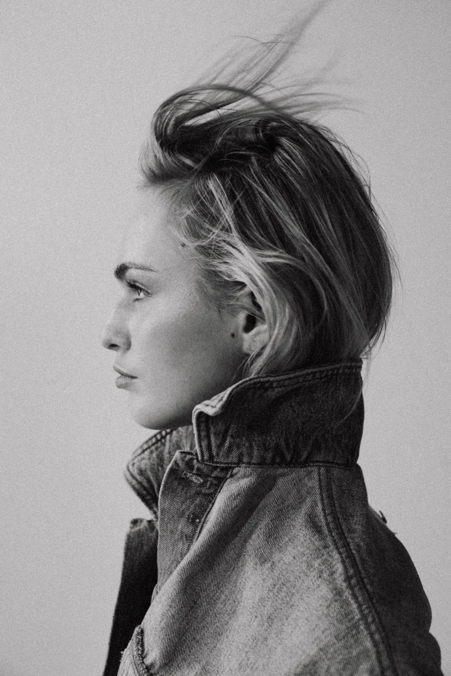 Side profile of a woman with short, tousled hair wearing a denim jacket