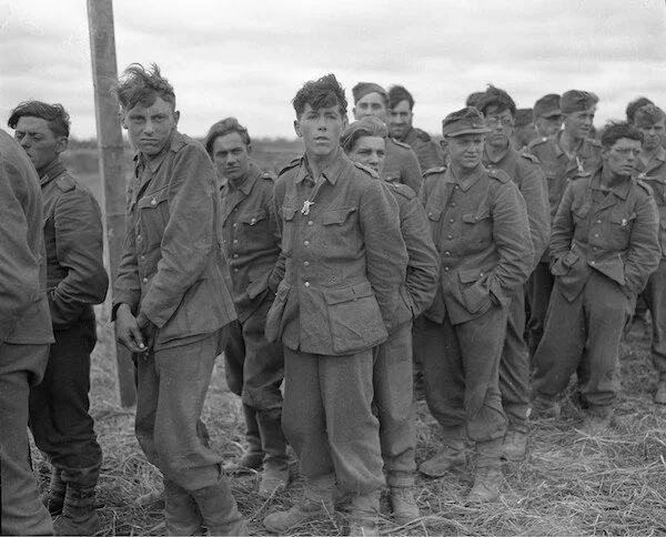 Black and white photo of young soldiers standing in line outdoors, wearing military uniforms, with a cloudy sky in the background.