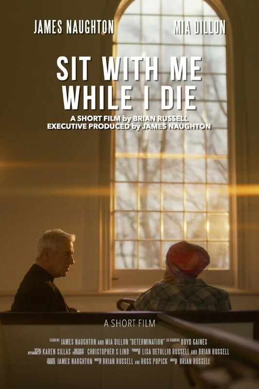 Poster for the short film 'Sit with Me While I Die' featuring James Naughton and Mia Dillon, showing a man and a woman sitting side by side in a room with large window and sunlight streaming in.