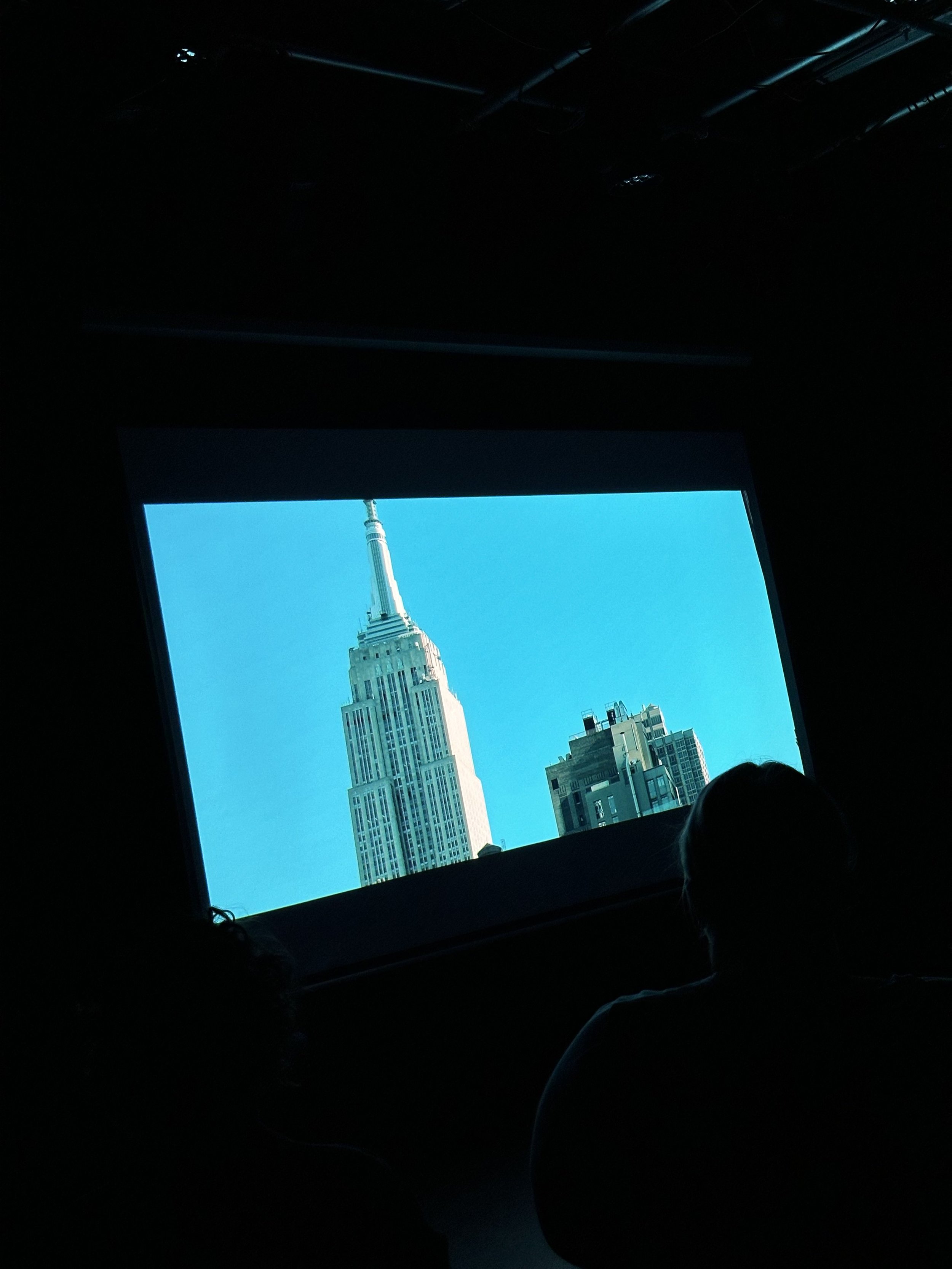 People watching a video of the Empire State Building on a screen in a dark room.