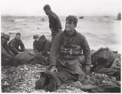 Group of African American men sitting and lying on a rocky beach, with one man sitting up and looking towards the camera.