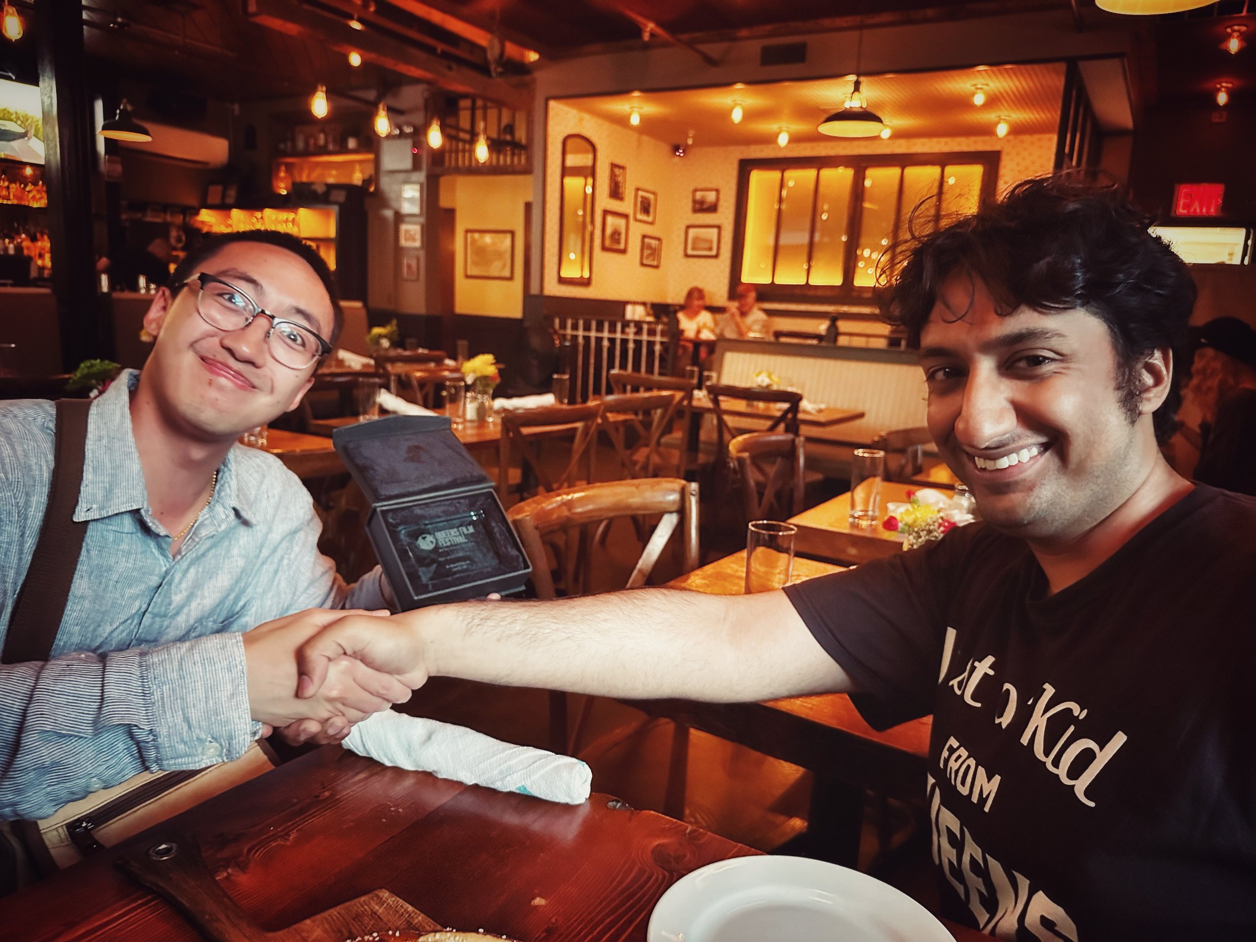 Two men shaking hands inside a restaurant, smiling at the camera.