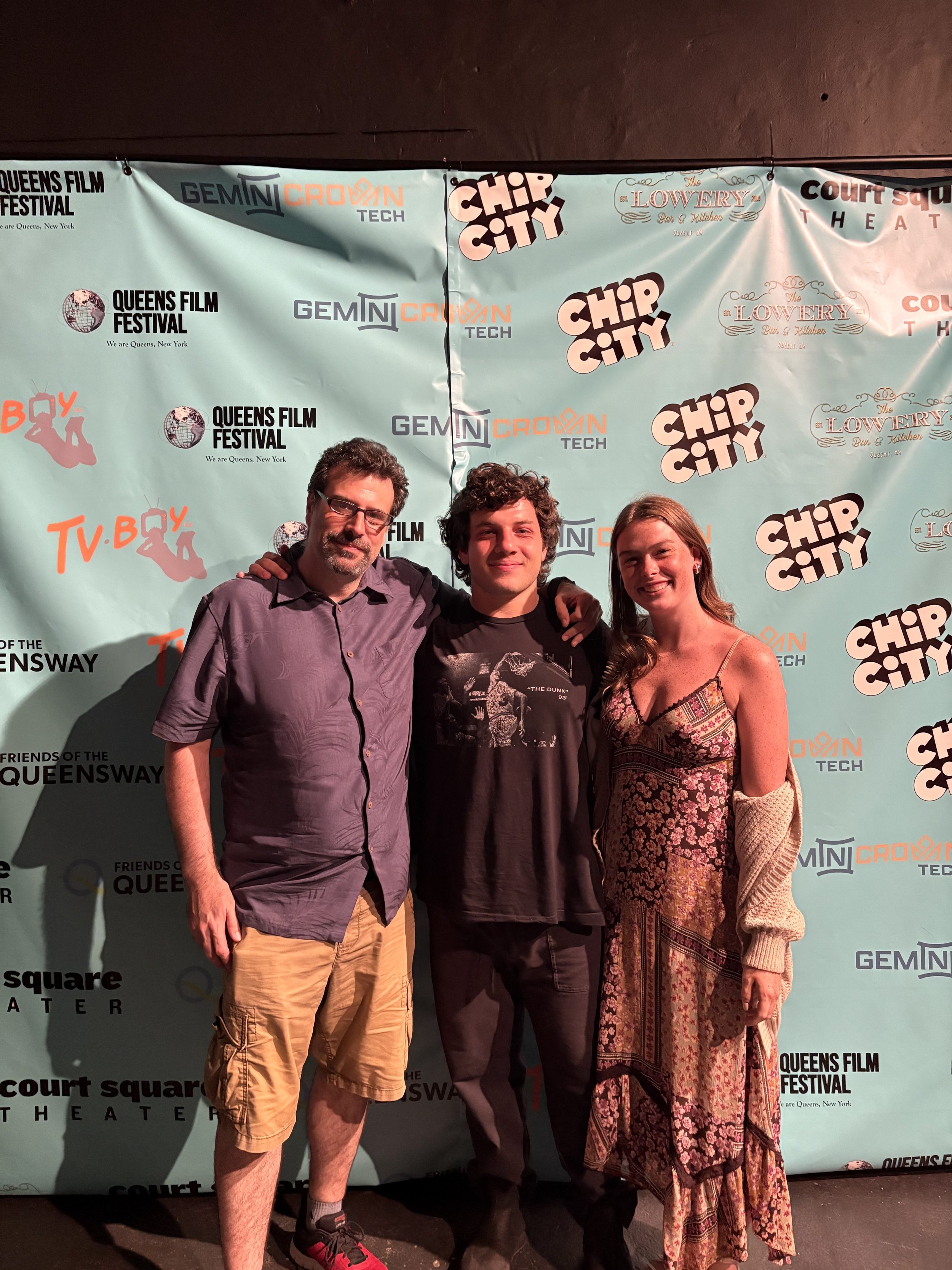Three people standing together at a film festival, posing for a photo in front of a step-and-repeat banner with various festival and sponsor logos.