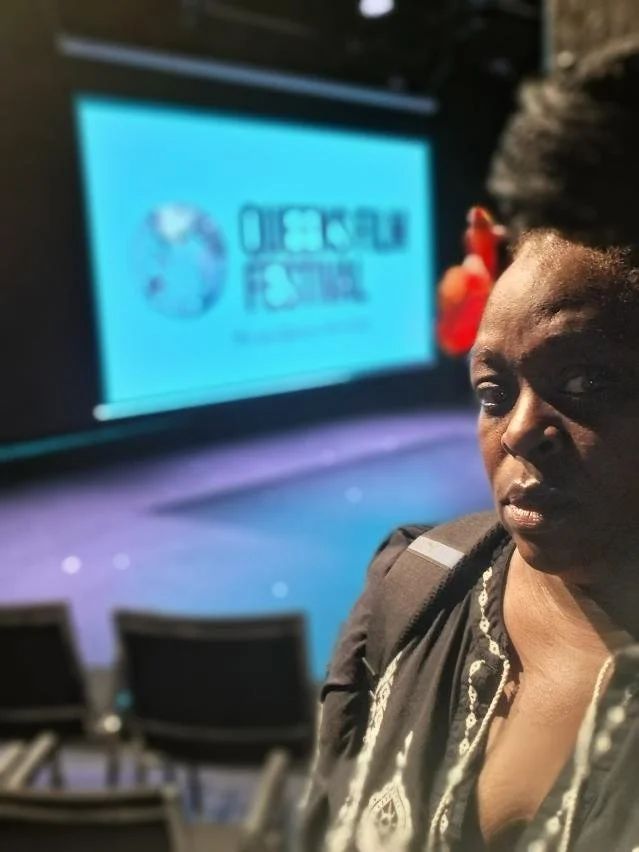 A woman taking a selfie in an auditorium with a large screen displaying the Dreamforce logo in the background.