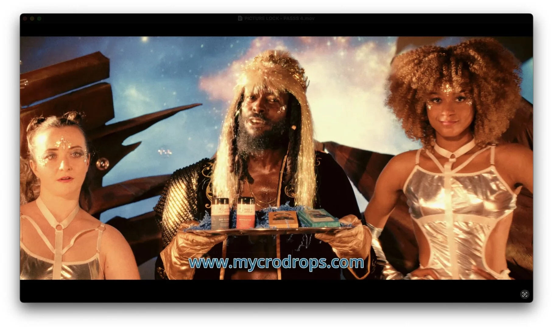 Three individuals in metallic outfits standing in front of a space-themed backdrop with a man holding a tray of pulsing lights, drinks, and small packages, with a website URL at the bottom.