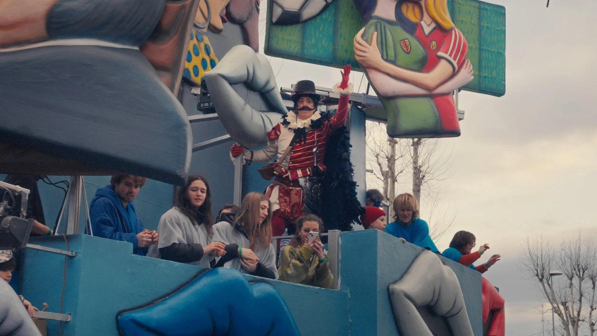 People on a parade float, with a person dressed as a historical figure in costume, surrounded by large colorful cartoon-like props and figures.