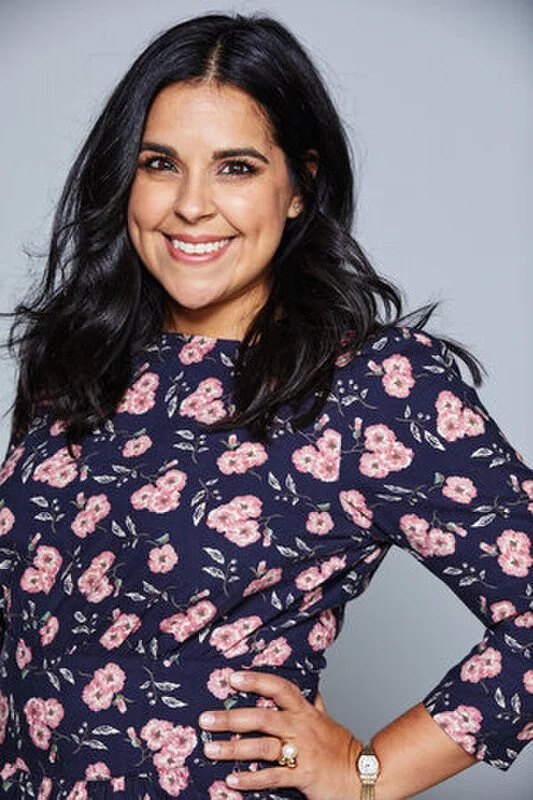 Smiling woman with dark hair in a floral navy blue dress posing with her hand on her hip