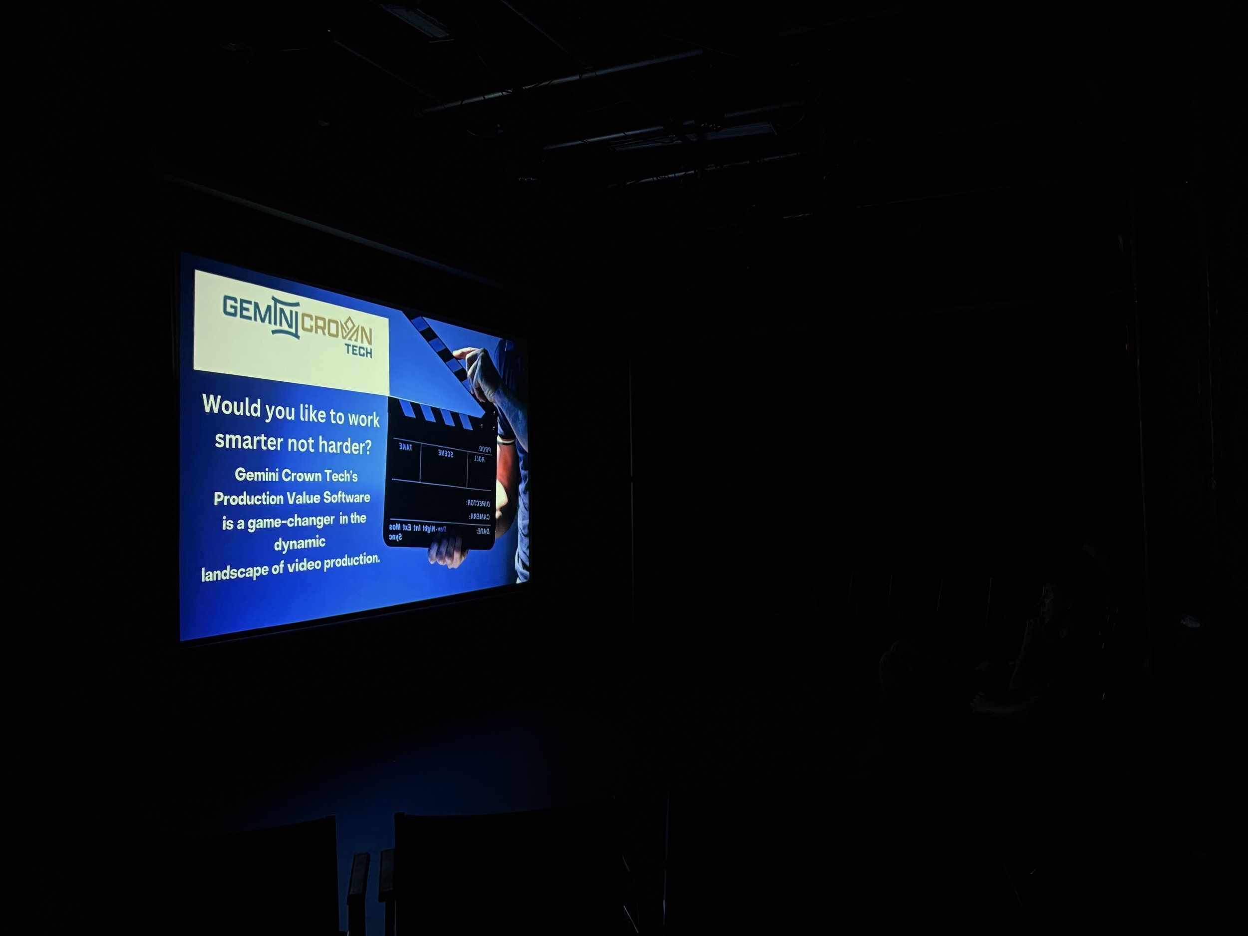 A presentation slide in a dark room, featuring the Gemini Crown Tech logo, a person holding a tablet, and text promoting Gemini Crown Tech's production software as a game-changer in video production.