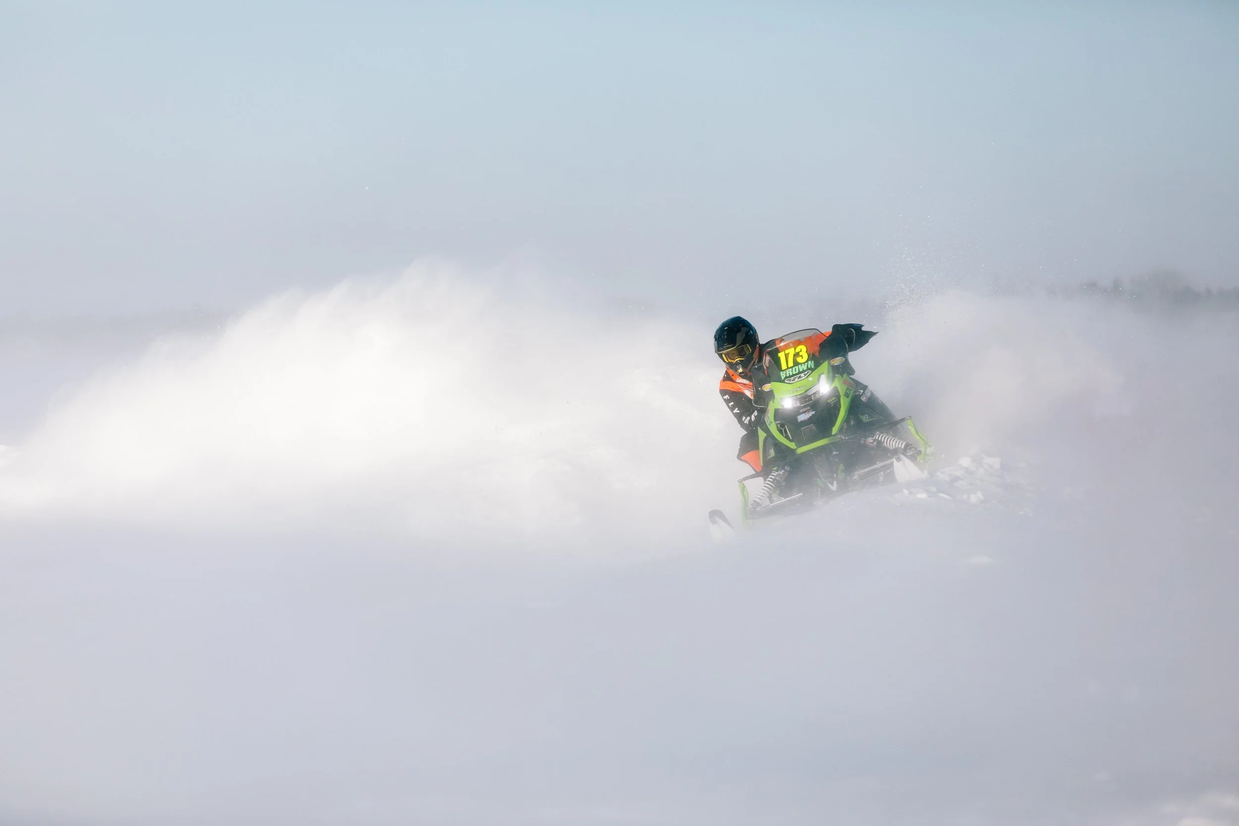 A snowmobile racer going around a curve with snow blowing around