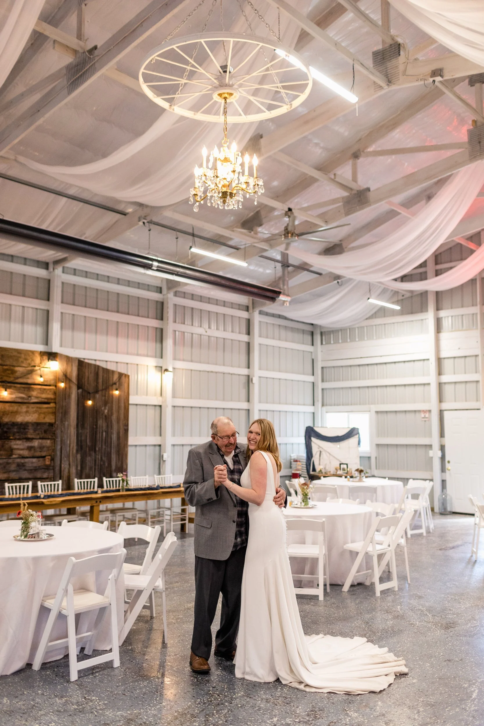 Wide shot of bride dancing with her granfather in a white banquet hall interior underneath a chandelier