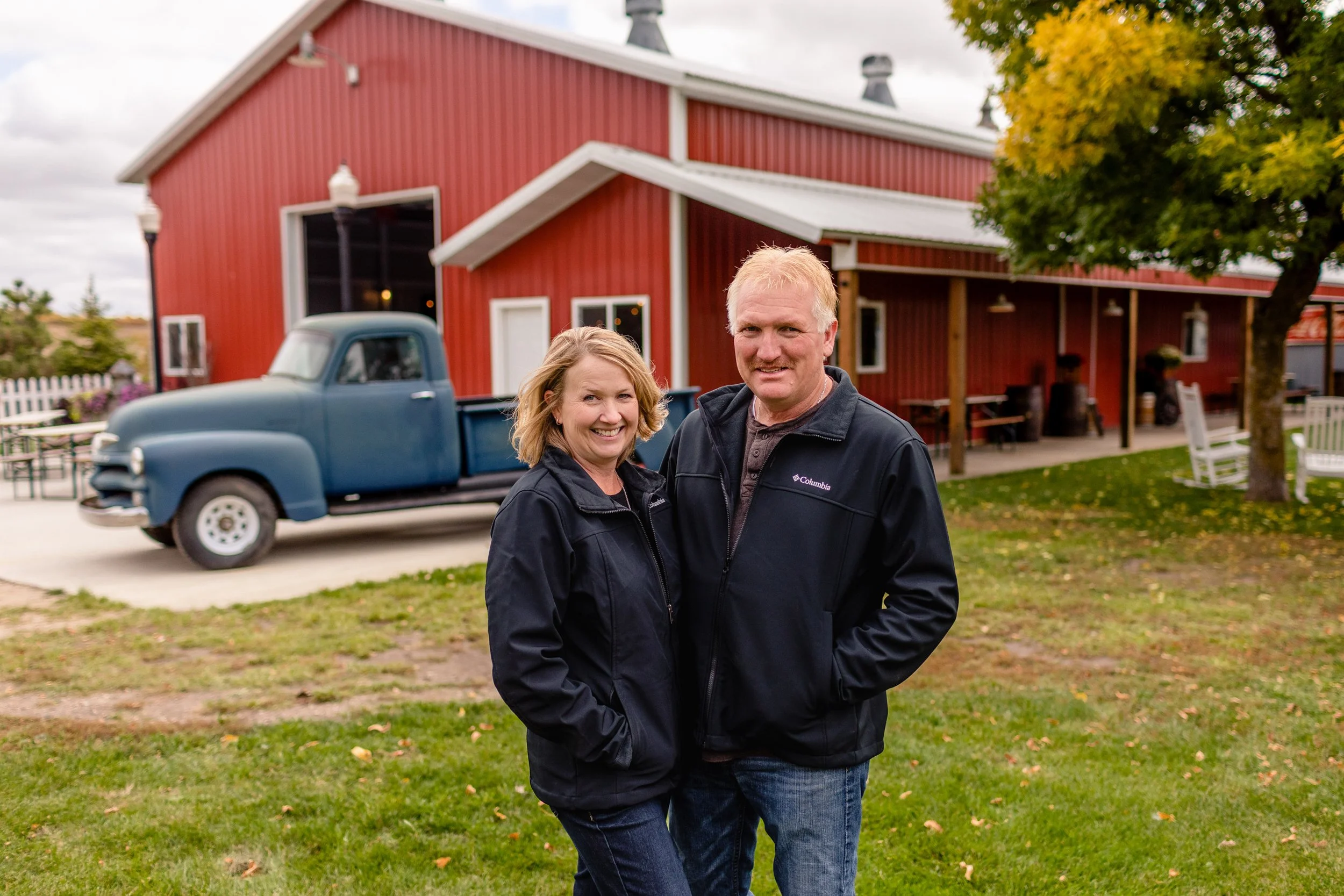 Photograph of venue owners infront of a vintage blue truck and red banquet hall