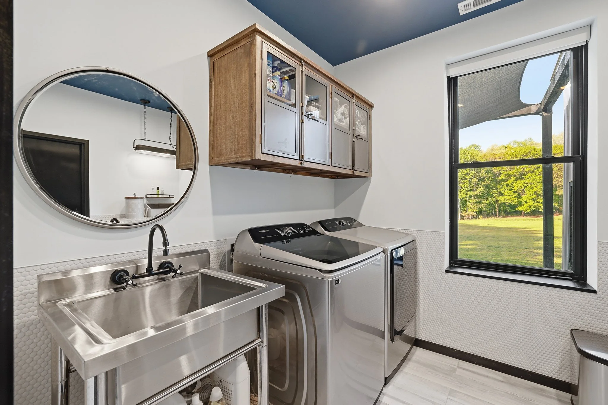 The room laundry features a Samsung side-by-side washer and dryer team with a utility sink, ample storage, and penny tile wainscoting 