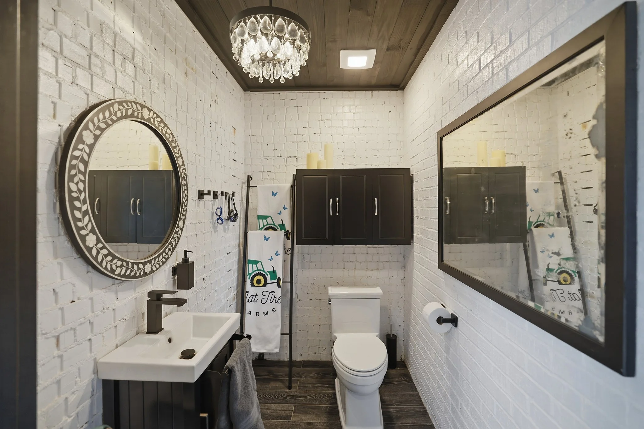 The pool house half-bath features elegant mirrors, beautifully painted exposed brick, ample storage, and a stylish sink