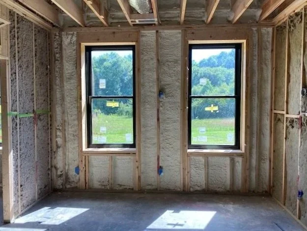 Interior of a house under construction with two new windows, exposed wooden framing, and insulation in the walls.