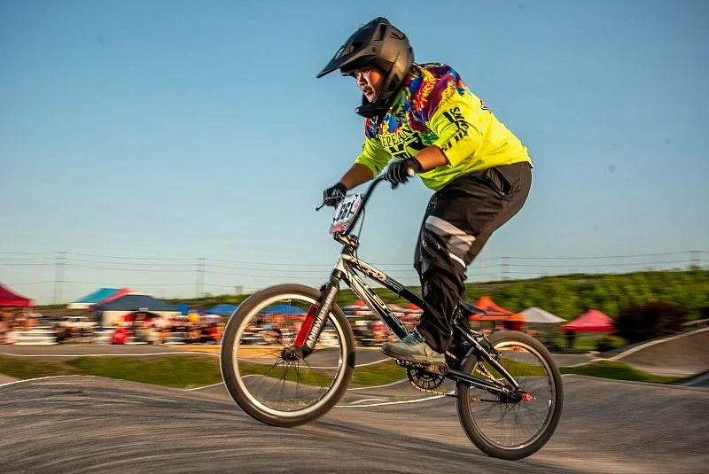 BMX rider wearing a helmet and colorful jersey performing a jump on a dirt track.