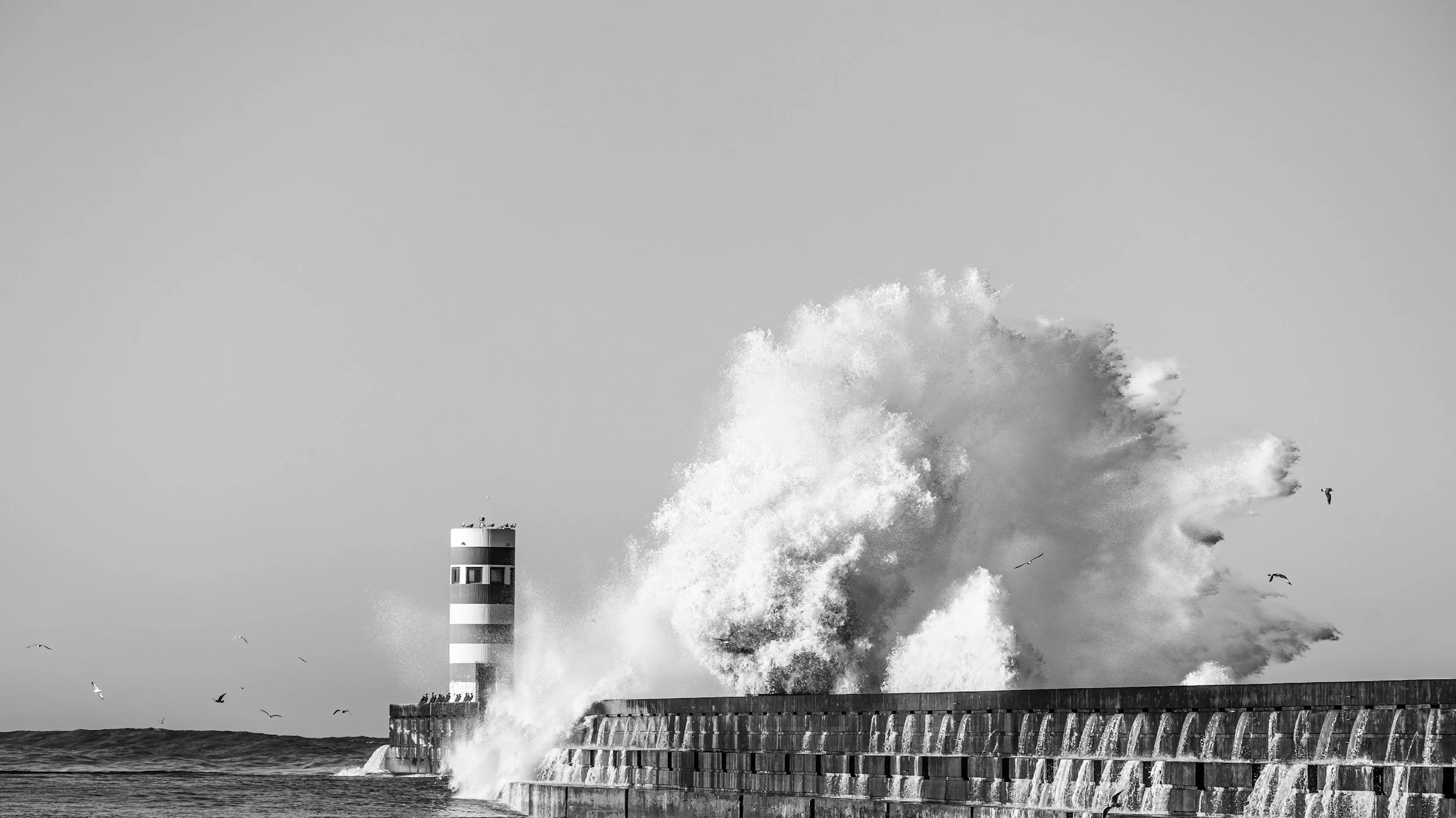 A high sea wave hitting the lighthouse and the wall dam