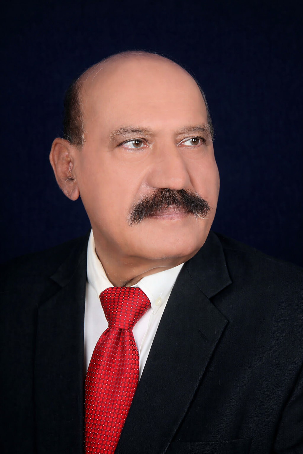 (Retd) Brig Dr Ahmed RAshid Wearing a black suit, white shirt and red tie