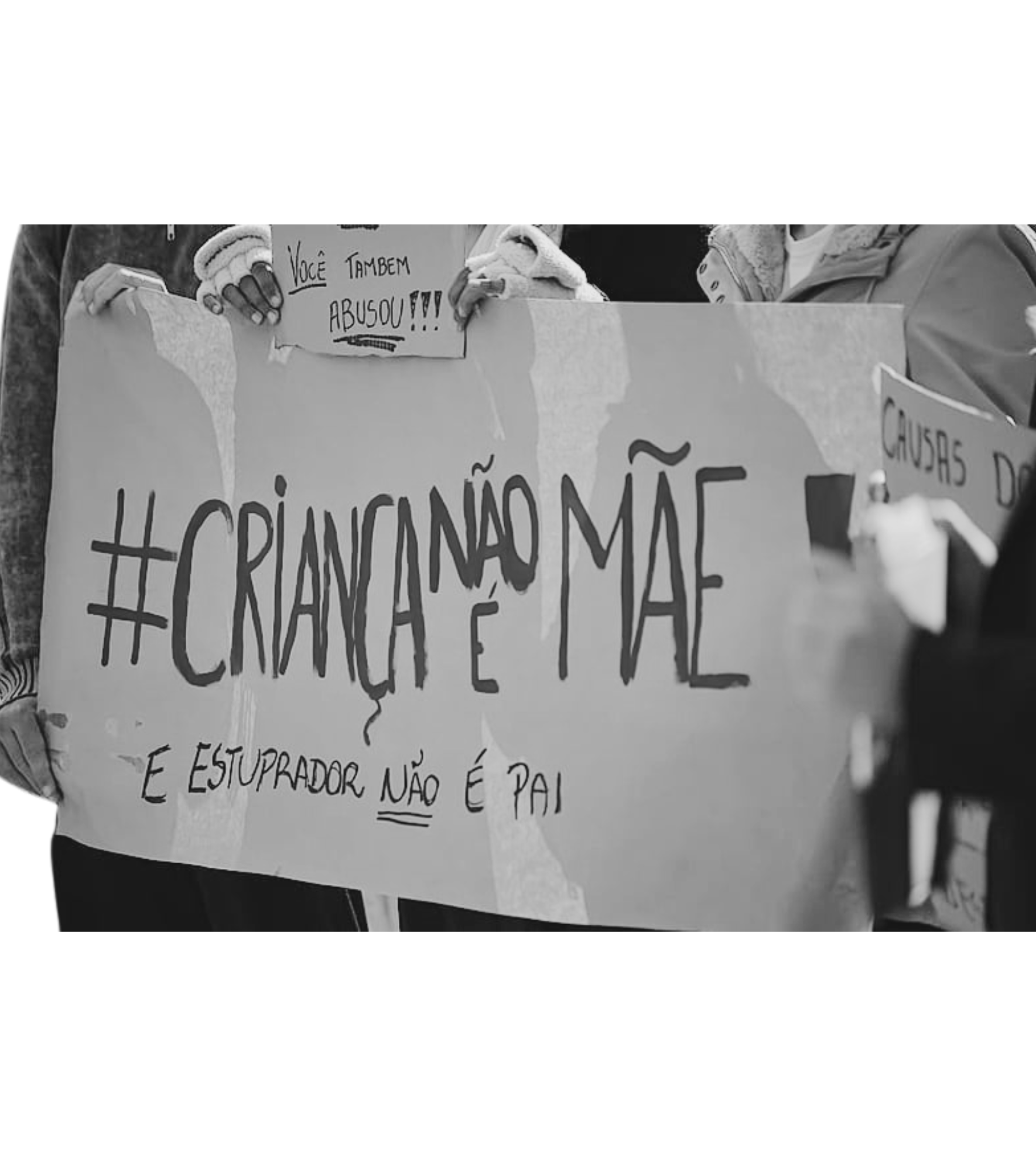 Pessoas segurando cartaz com mensagem de protesto, incluindo hashtags e frases em português.