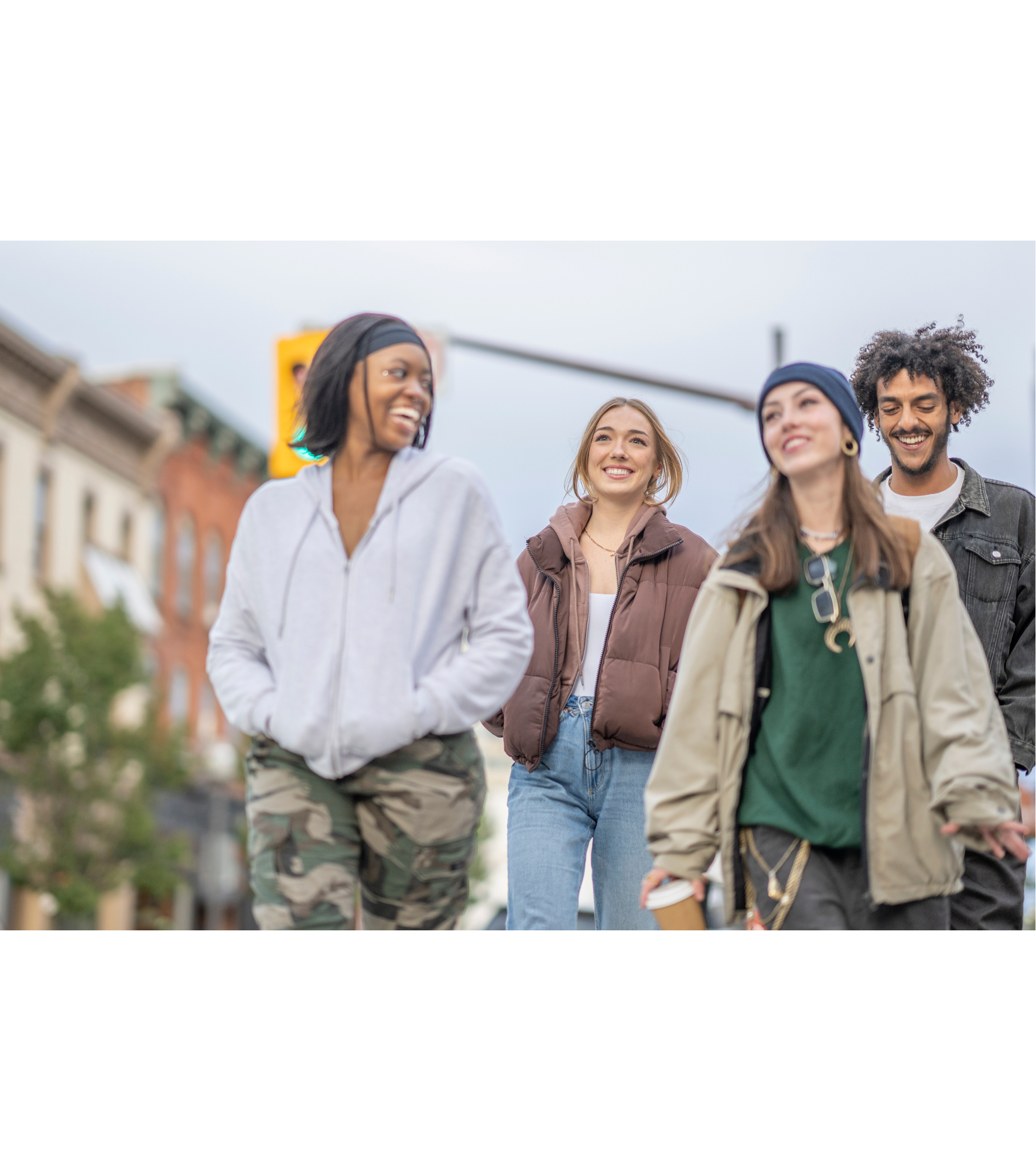 Quatro jovens caminhando e conversando na rua, sorrindo, com prédios ao fundo.