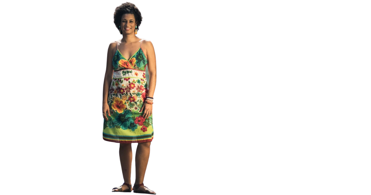 Mulher de cabelos curtos e cacheados, vestindo um vestido de verão com estampa colorida de flores e folhas, posando sorridente com uma expressão feliz.