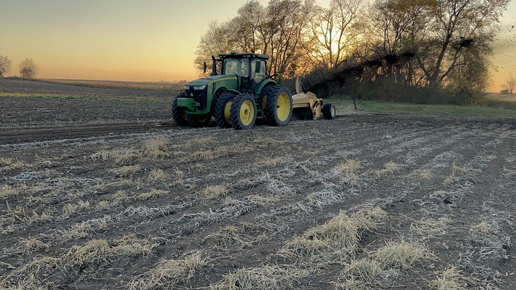 Tractor and implement working a field at sunset