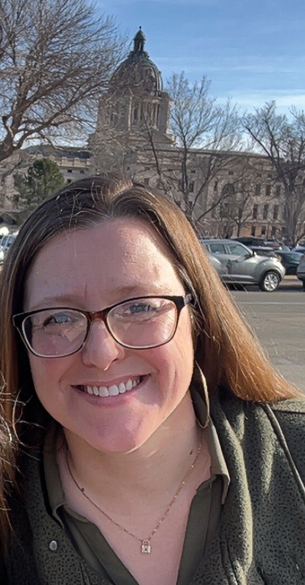 Smiling white woman with long brown hair and glasses.