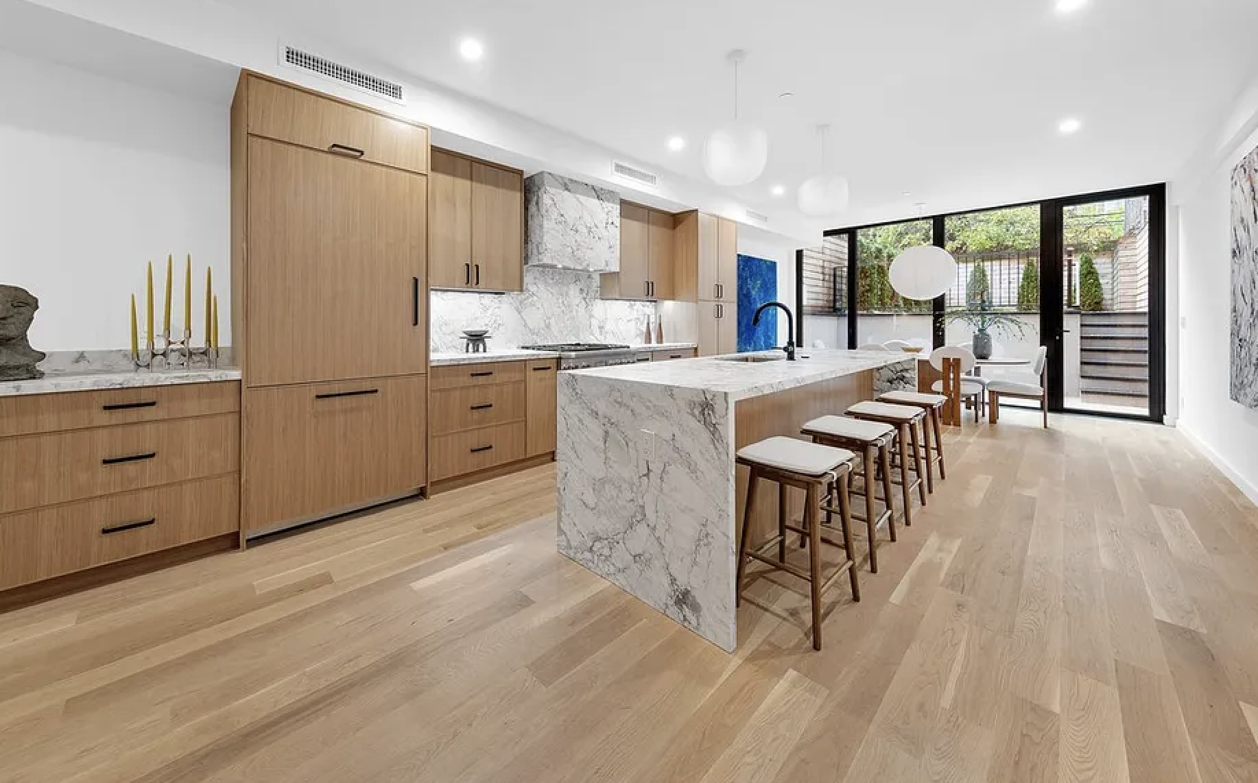 Modern kitchen with wooden cabinets, white marble island, and large glass sliding doors leading to an outdoor patio.