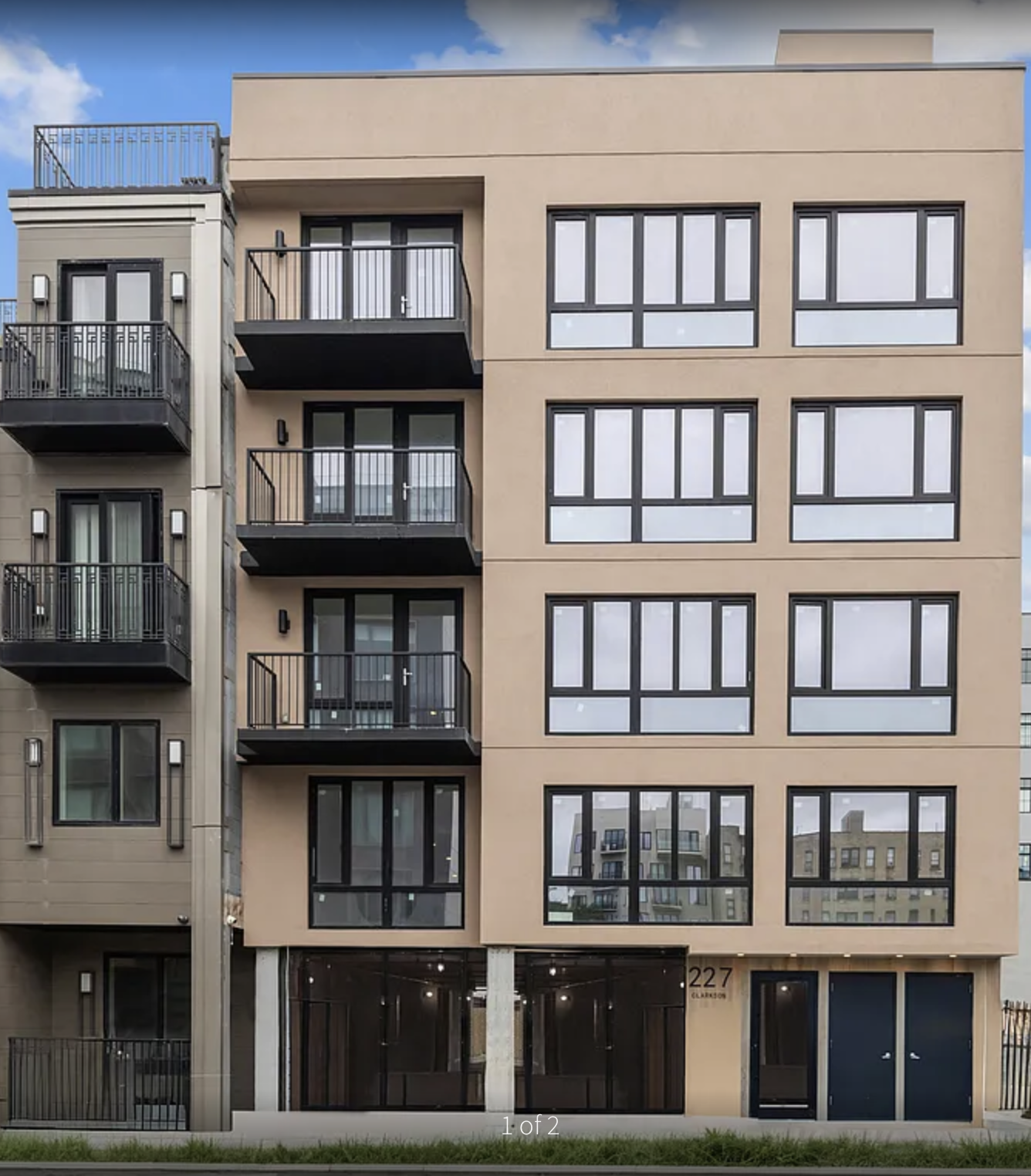 Exterior of a modern, six-story apartment building with large windows and balconies on the upper floors, and a ground-level entrance with black doors and a sign showing the number 227.