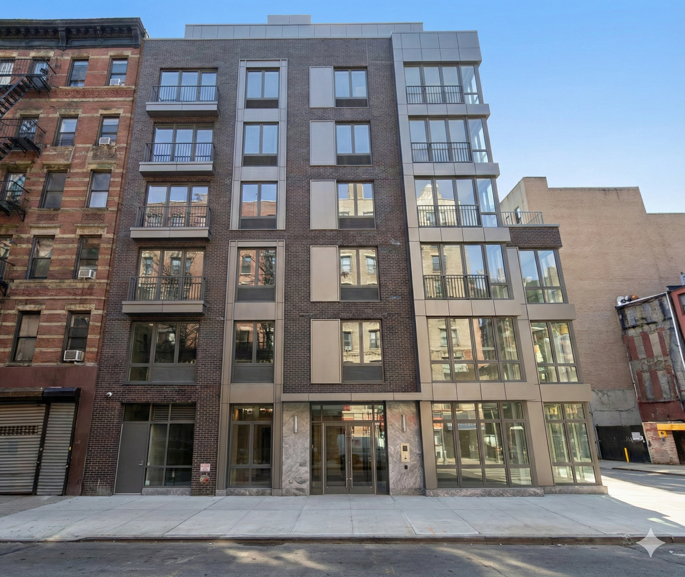 Modern multi-story apartment building with glass balconies and brick exterior, located in an urban setting on a city street.