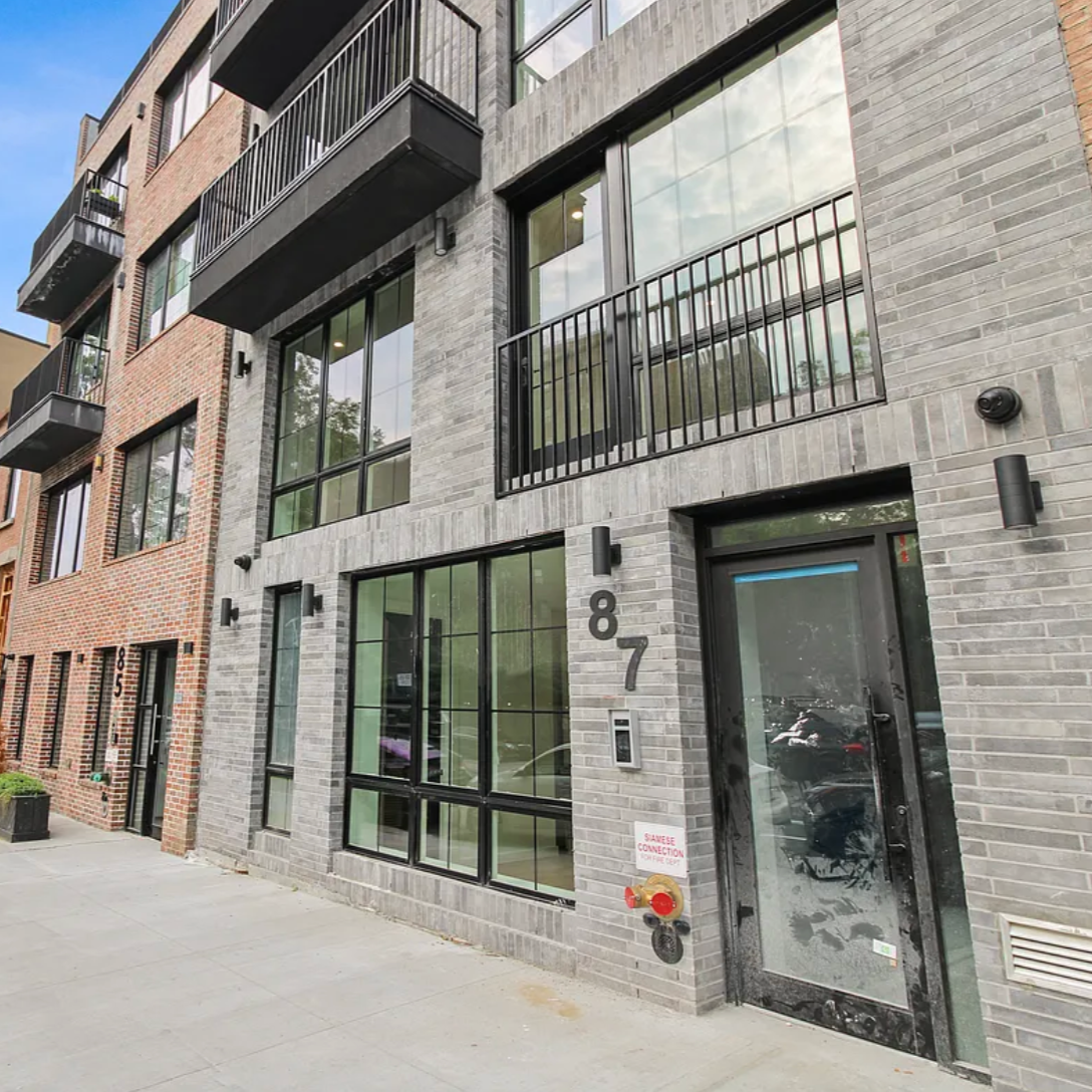 Modern apartment building with large windows and small balconies, located on a city street.