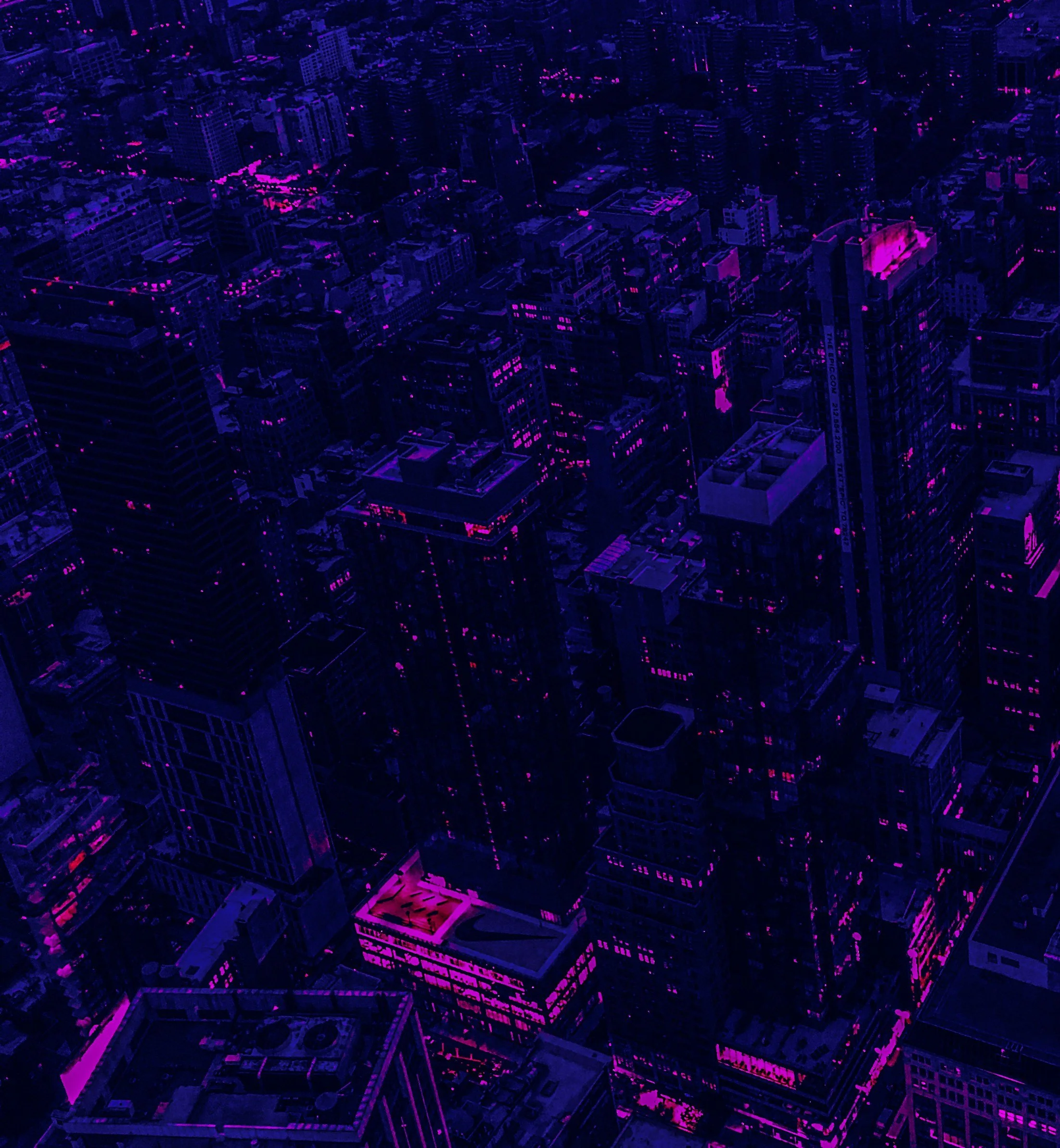 Nighttime aerial view of a city with tall buildings illuminated in shades of purple and pink.