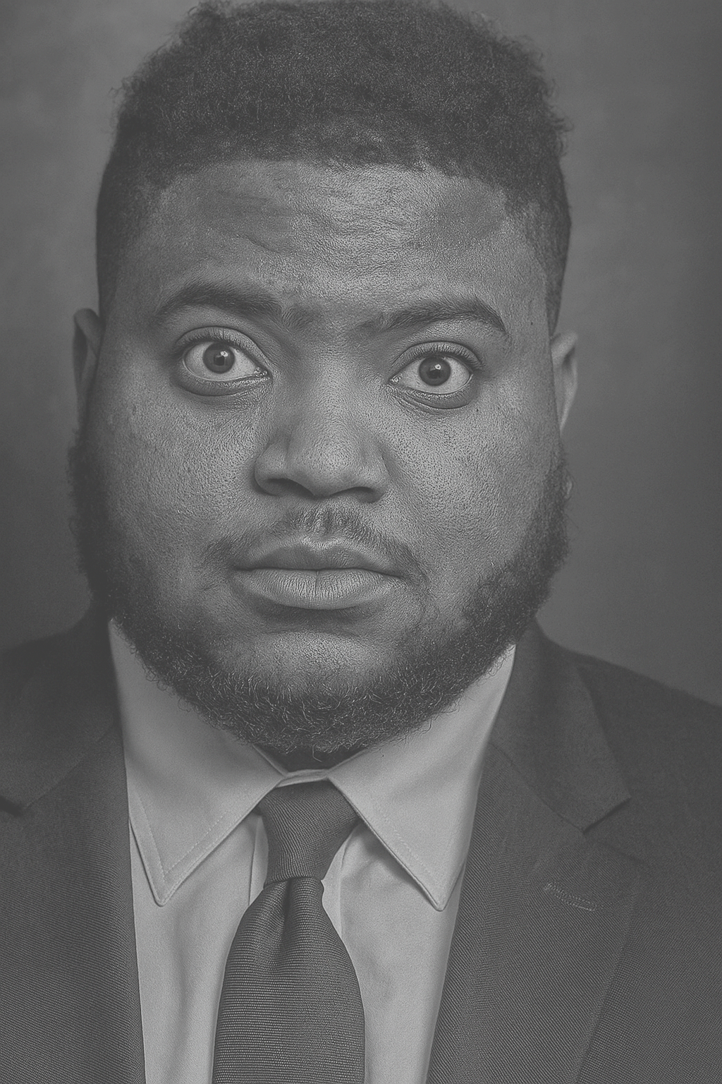 Black and white portrait of a man with a serious expression, wearing a suit and tie, looking directly at the camera.