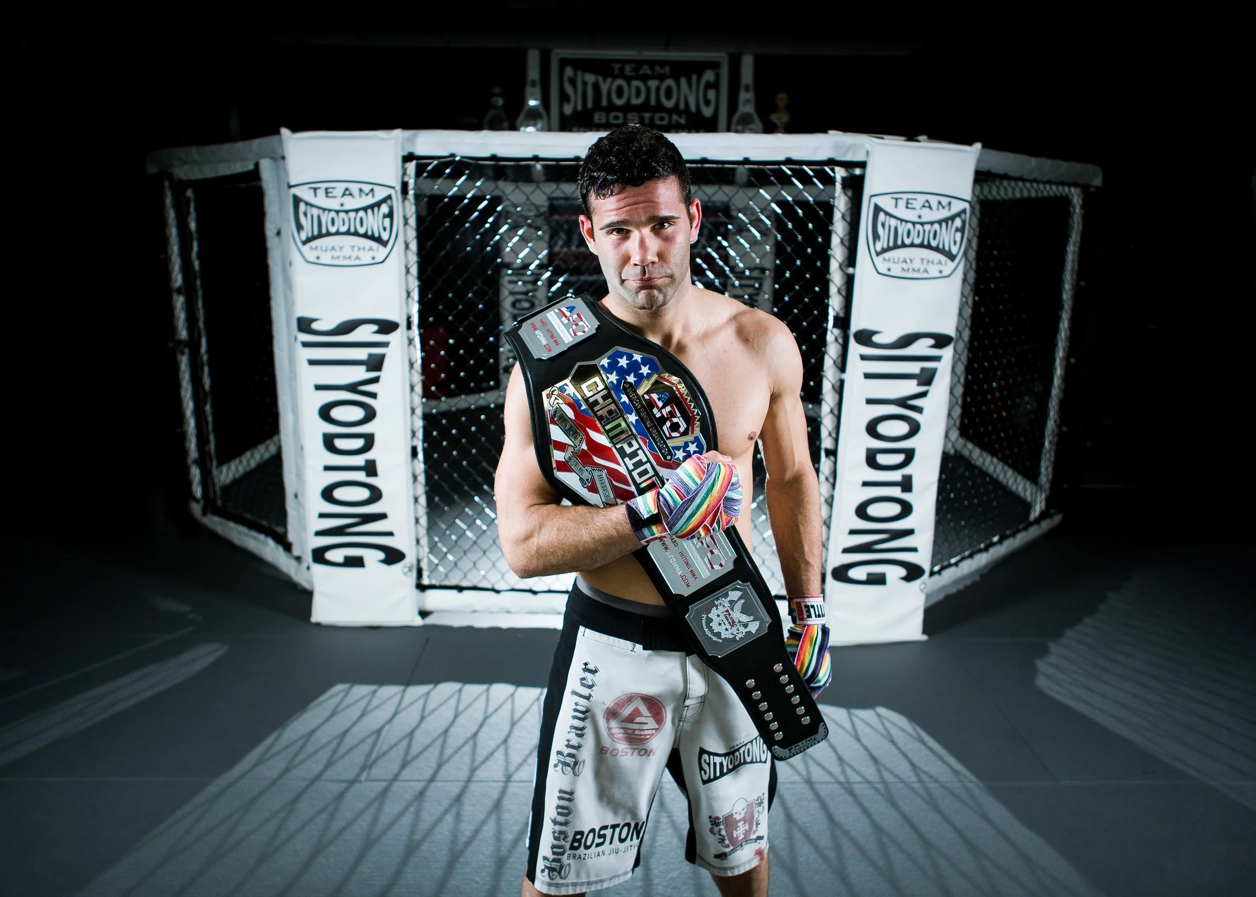 MMA fighter stands with belt in front of cage