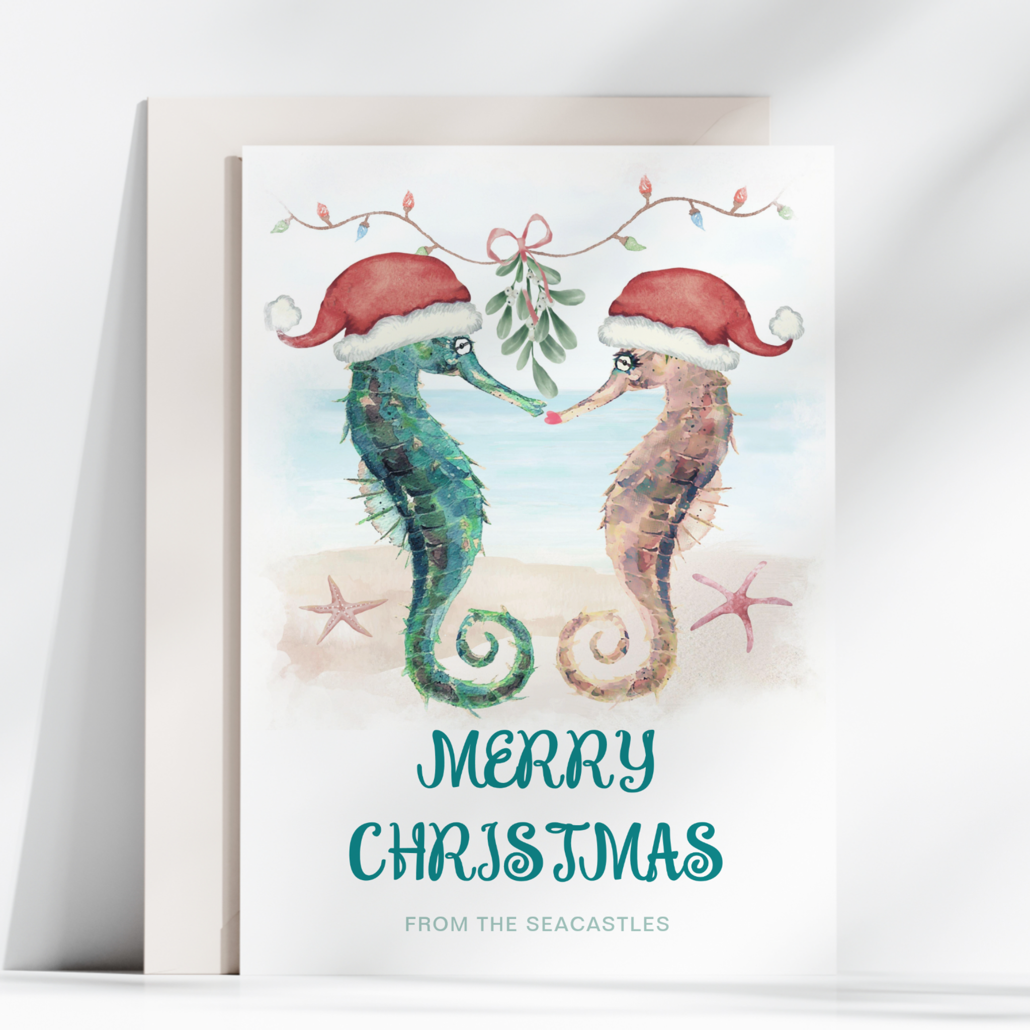 Watercolor coastal Christmas card featuring two seahorses wearing Santa hats sharing a kiss beneath mistletoe on a tropical beach.