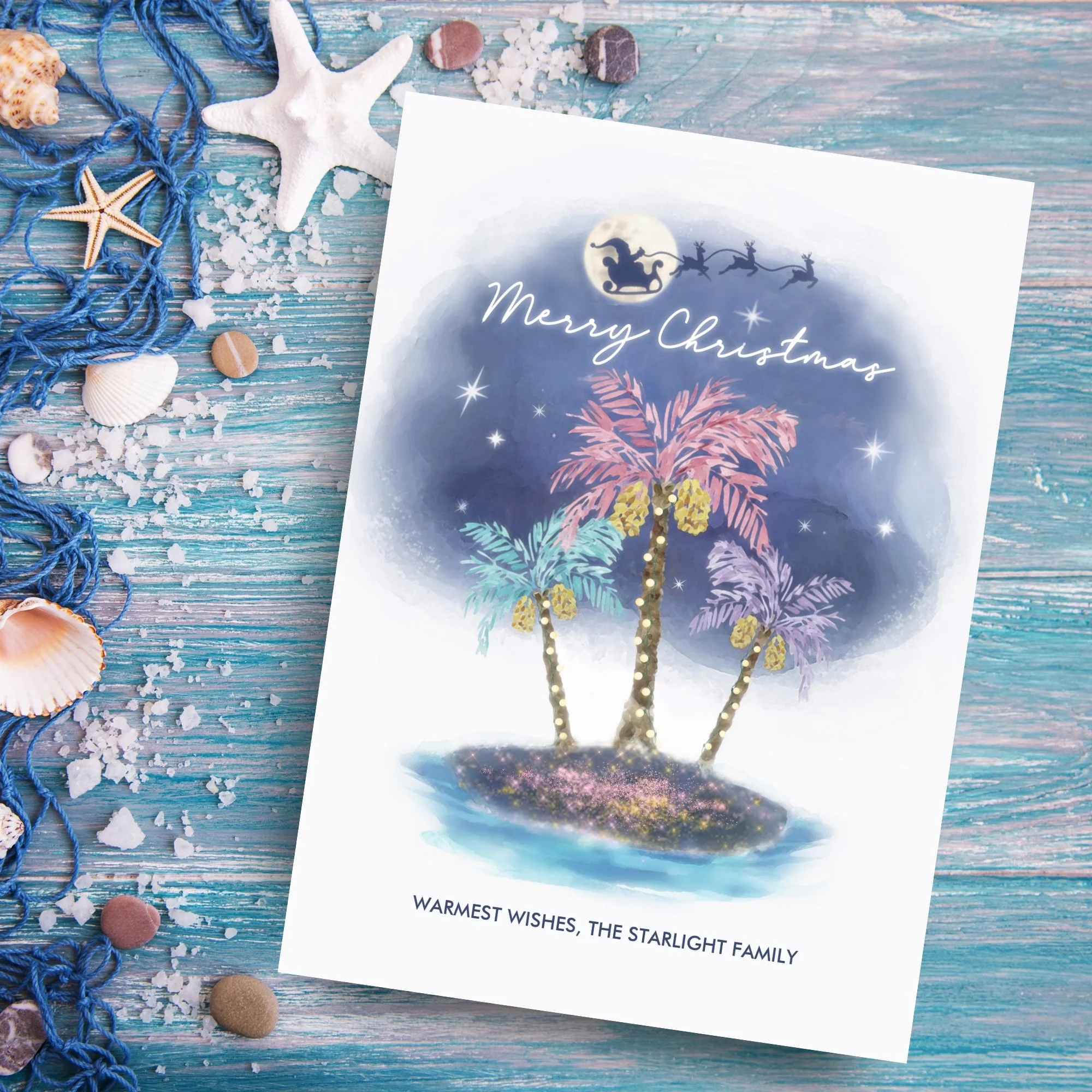 Tropical beach Christmas card featuring a sparkling sandy island, palm trees wrapped in holiday lights, and Santa with his reindeer flying across a moonlit sky above the ocean.
