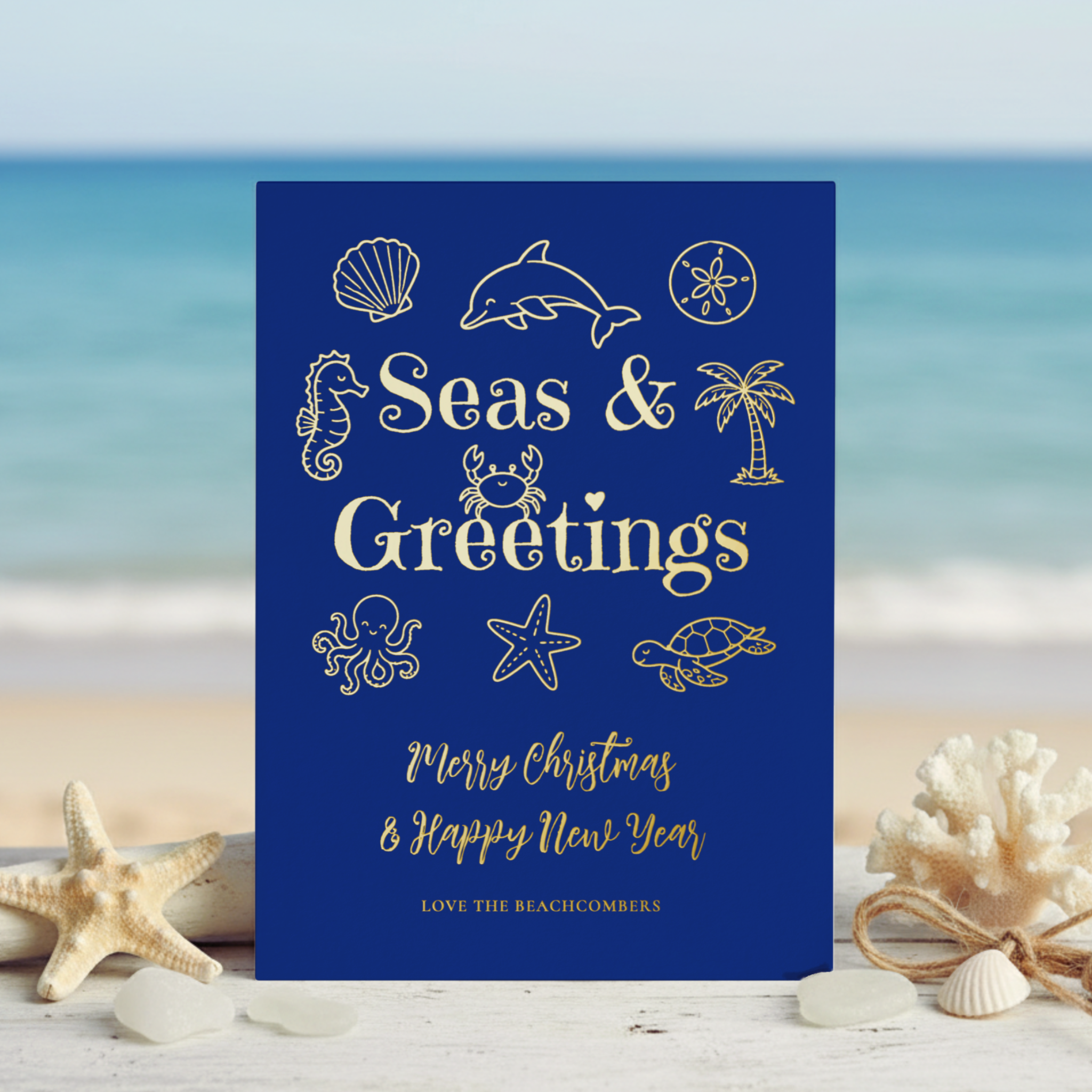 Gold foil Seas & Greetings coastal Christmas card featuring whimsical hand-drawn palm tree, seashells, starfish, dolphin, sea turtle, seahorse, octopus and crab on a navy blue background.