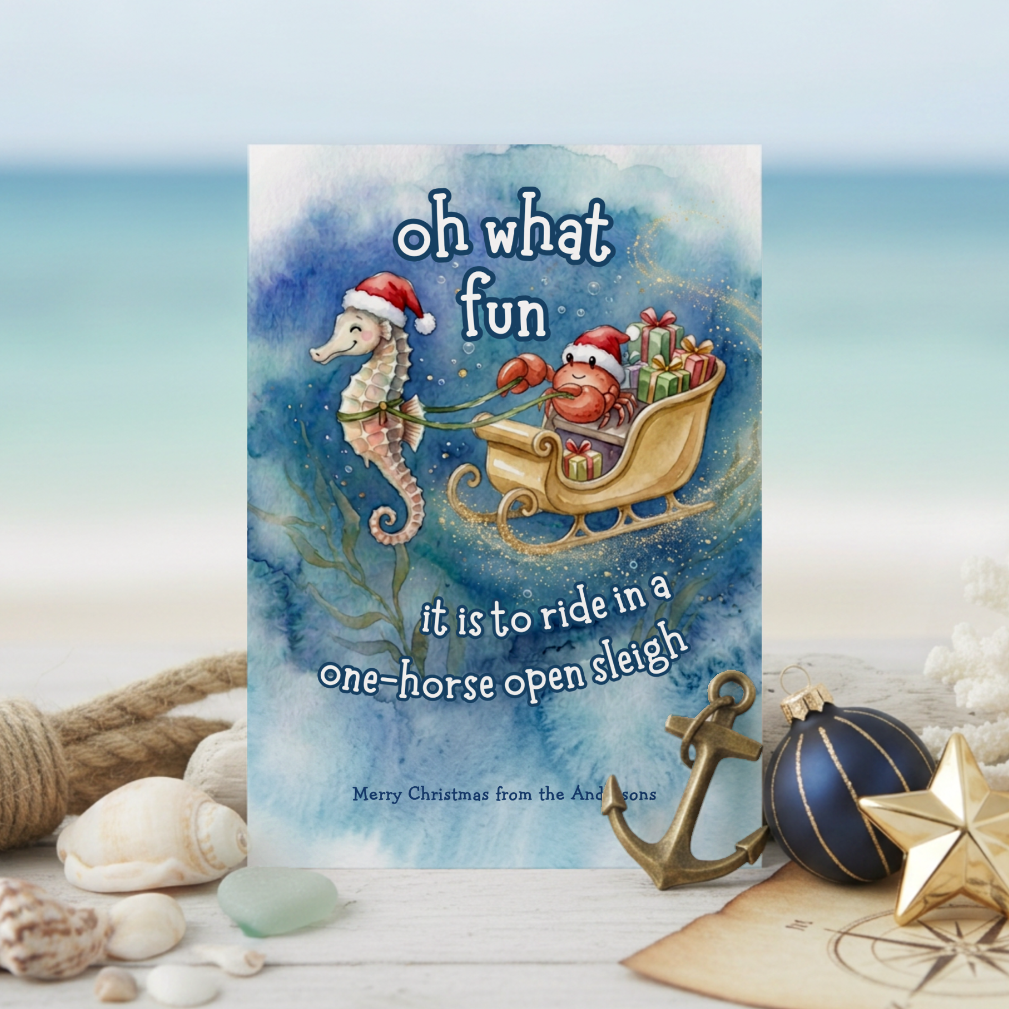 Watercolor coastal Christmas card featuring a seahorse pulling an underwater sleigh with Santa Claws the crab in a Santa hat at the reins and a playful Jingle Bells inspired holiday greeting.