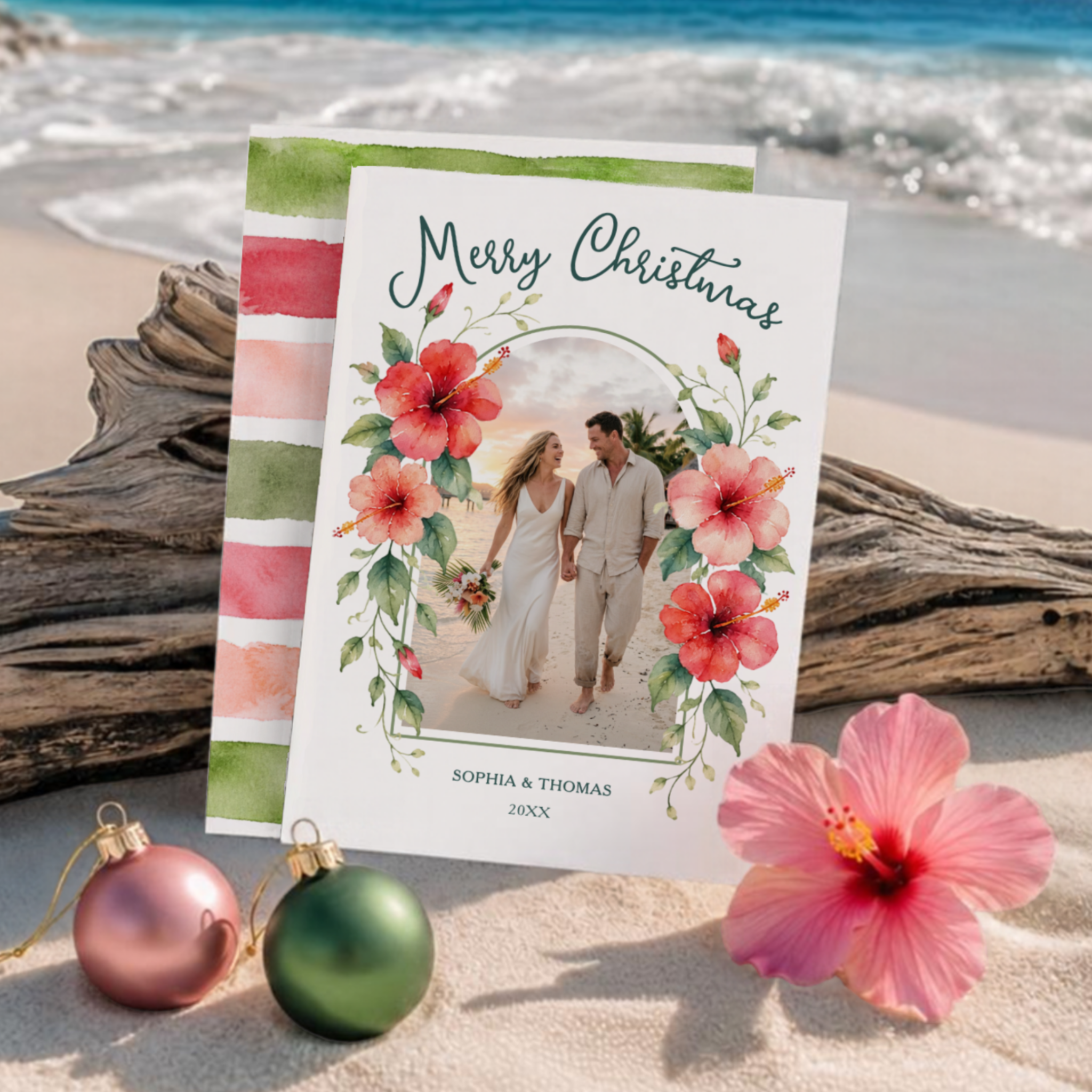 Watercolor tropical Christmas photo card with red, pink, and coral hibiscus flowers and green vines framing an arched photo area, a Merry Christmas greeting, customizable name and year, and coordinating watercolor stripes on the reverse.