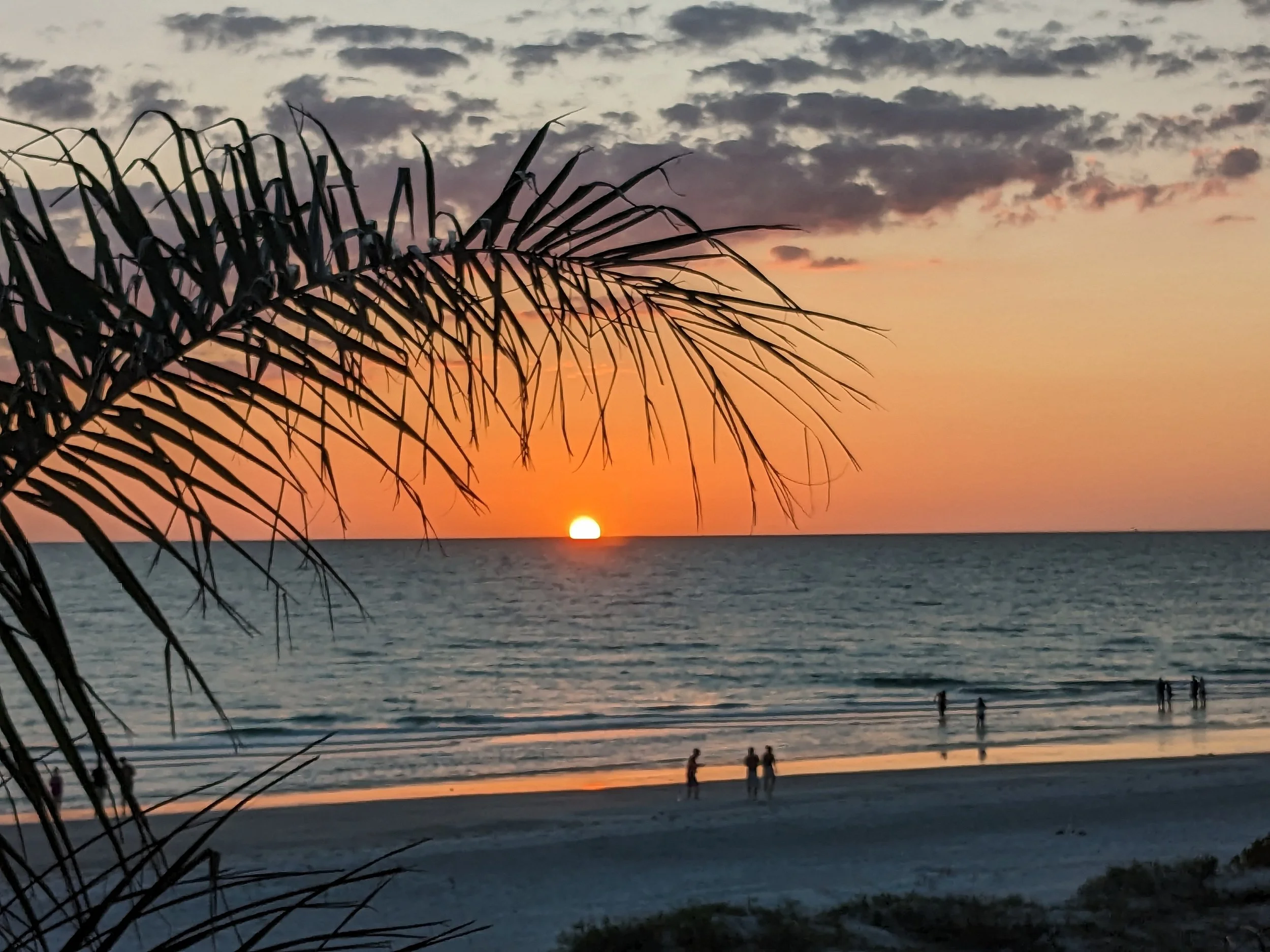 Colorful sunset over the ocean with waves crashing against rocks in the foreground.